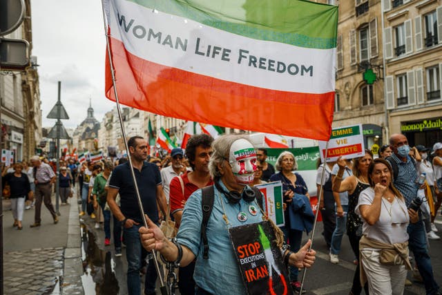 <p>A demonstrator carries a flag displaying with the colours of the Iranian flag reading ‘Woman Life Freedom' during a protest against the Iranian regime at Place de la Bastille in Paris on 16 September 2023</p>
