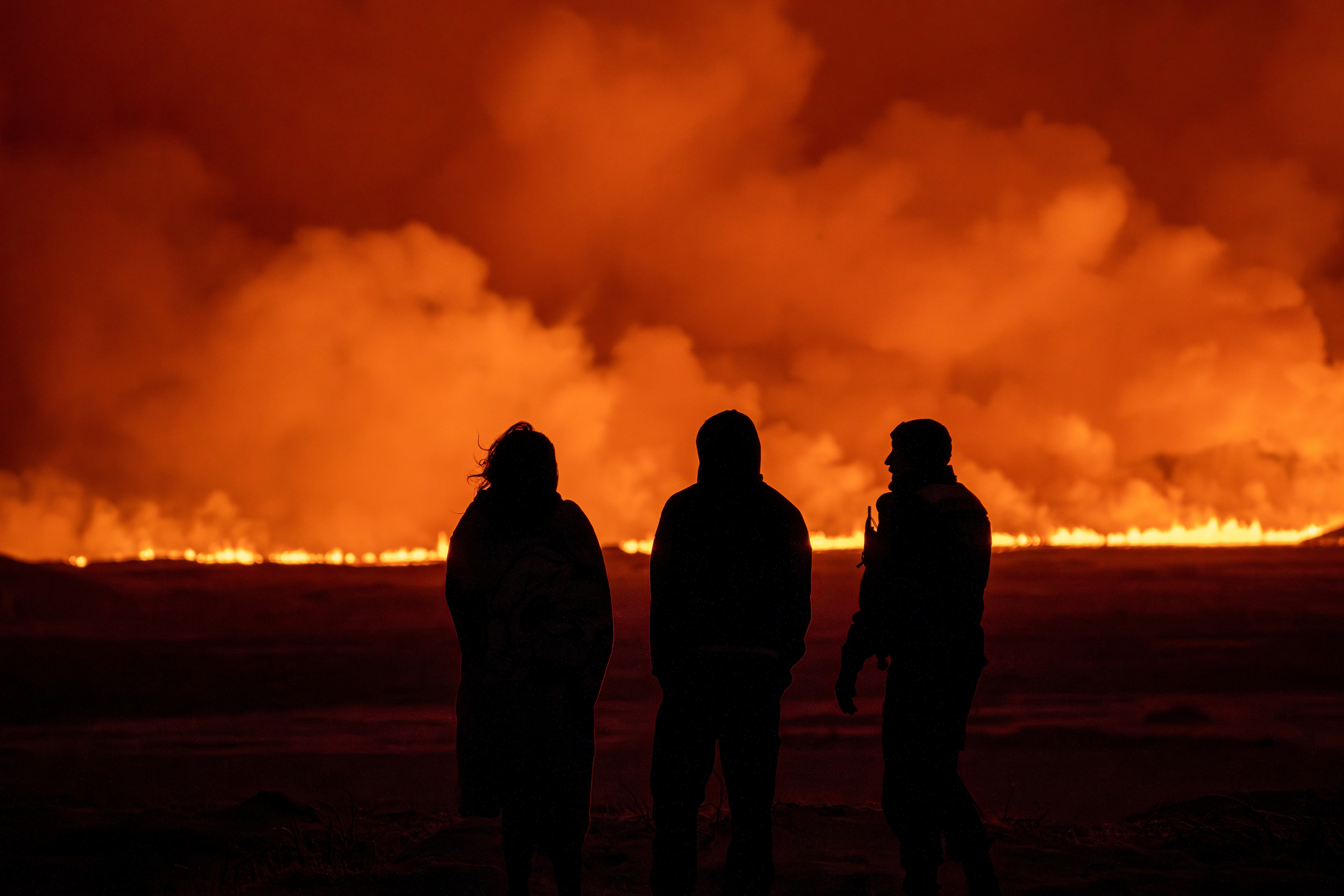 People watch as the night sky is illuminated caused by the eruption of a volcano in Grindavik on Iceland's Reykjanes Peninsula, Monday, Dec. 18, 2023