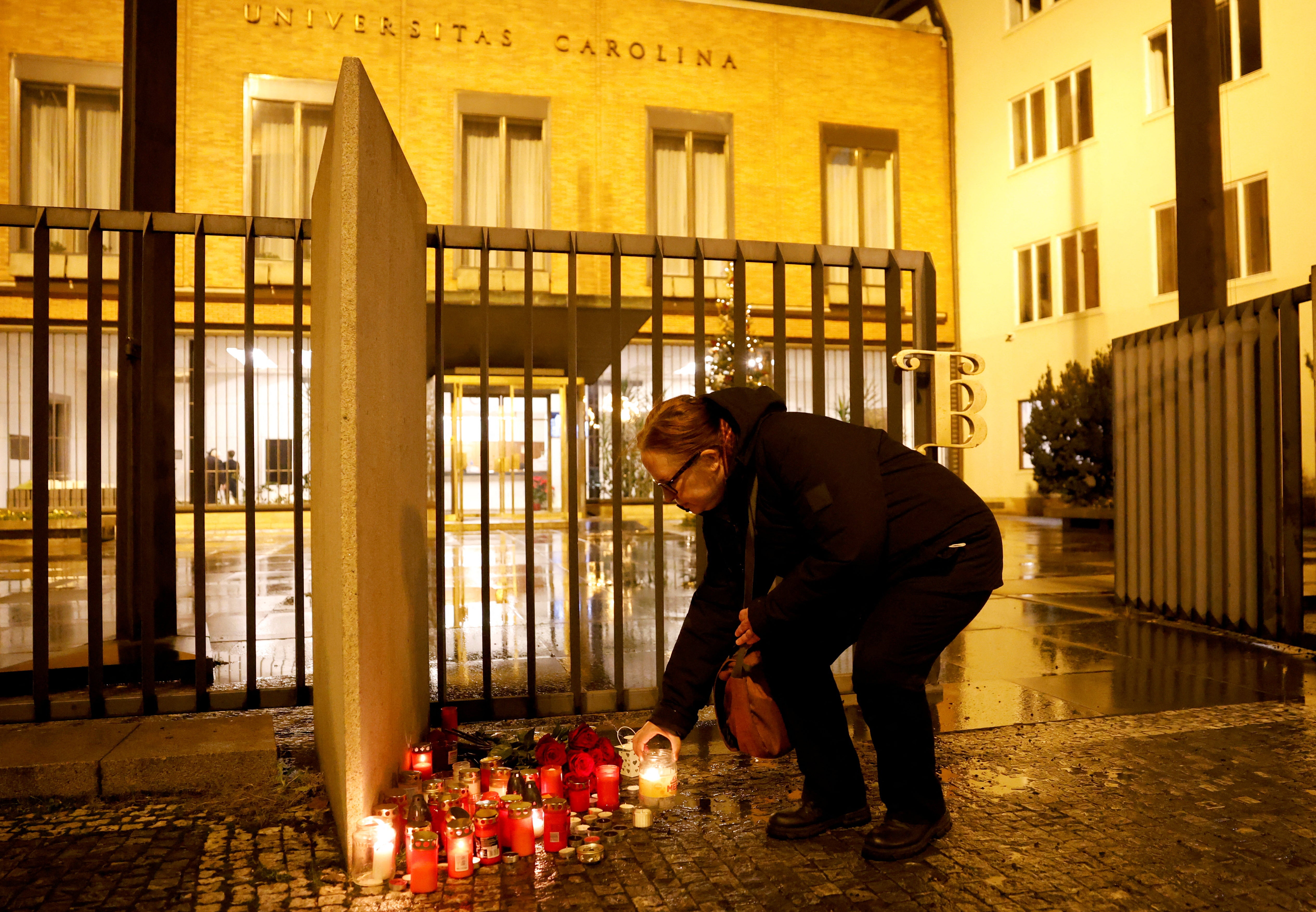 <p>A woman lights a candle in front of Charles University main building following the shooting</p>