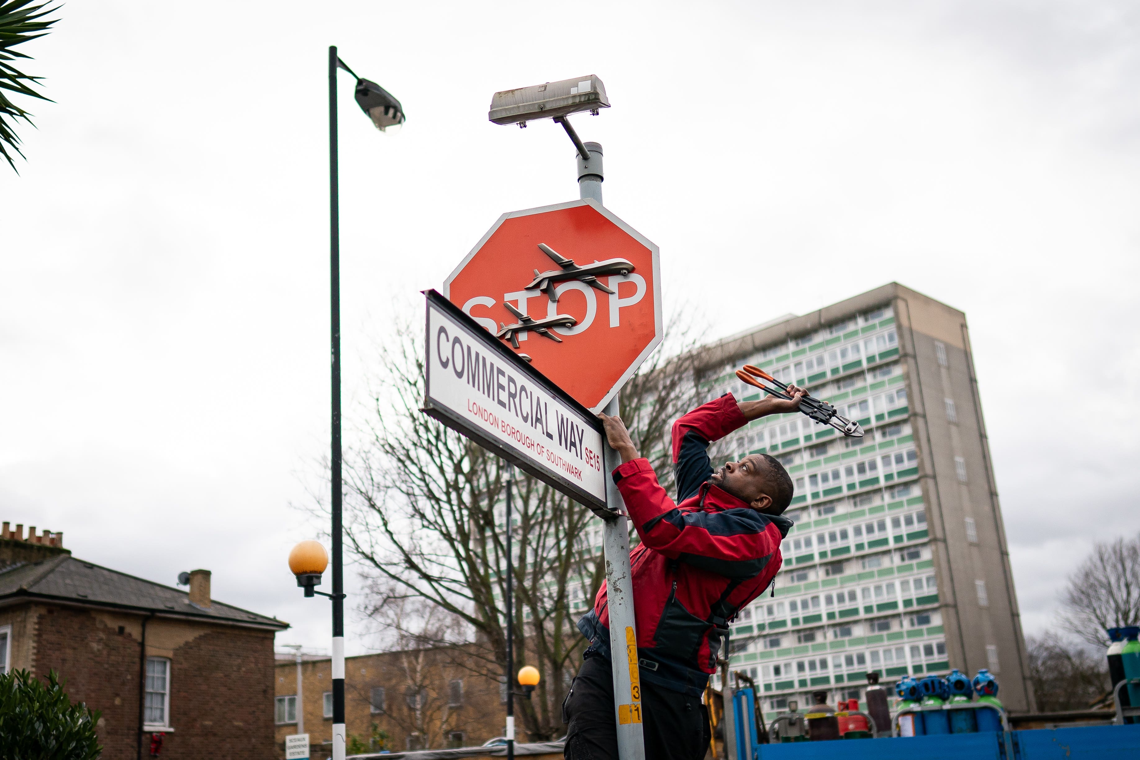 A man removes a piece of art by Banksy at the intersection of Southampton Way and Commercial Way in Peckham