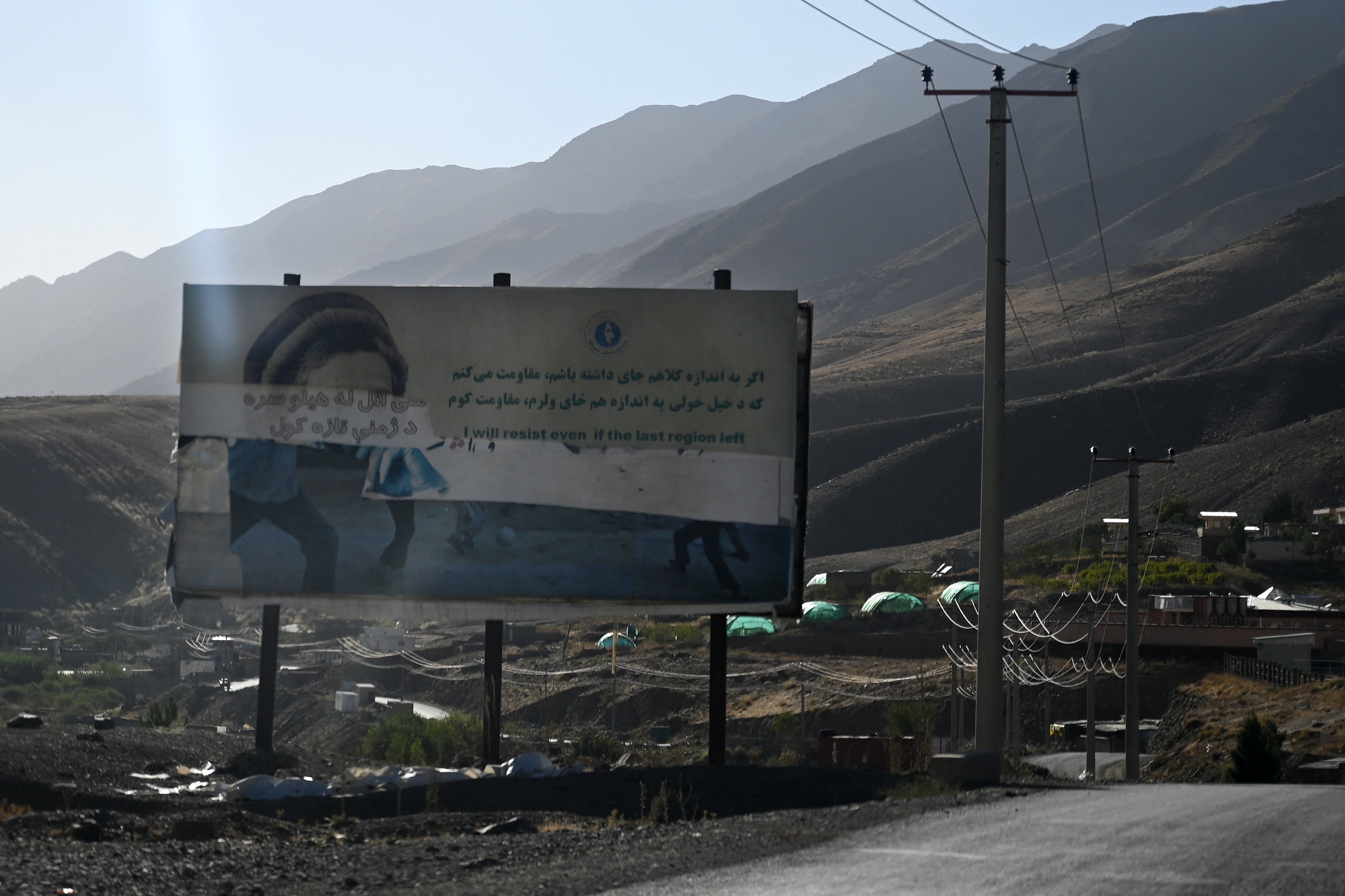 A destroyed poster depicts the late Afghan Mujahideen leader Ahmad Shah Massoud alongside a message about resistance, on a roadside near Dashtak in Panjshir province