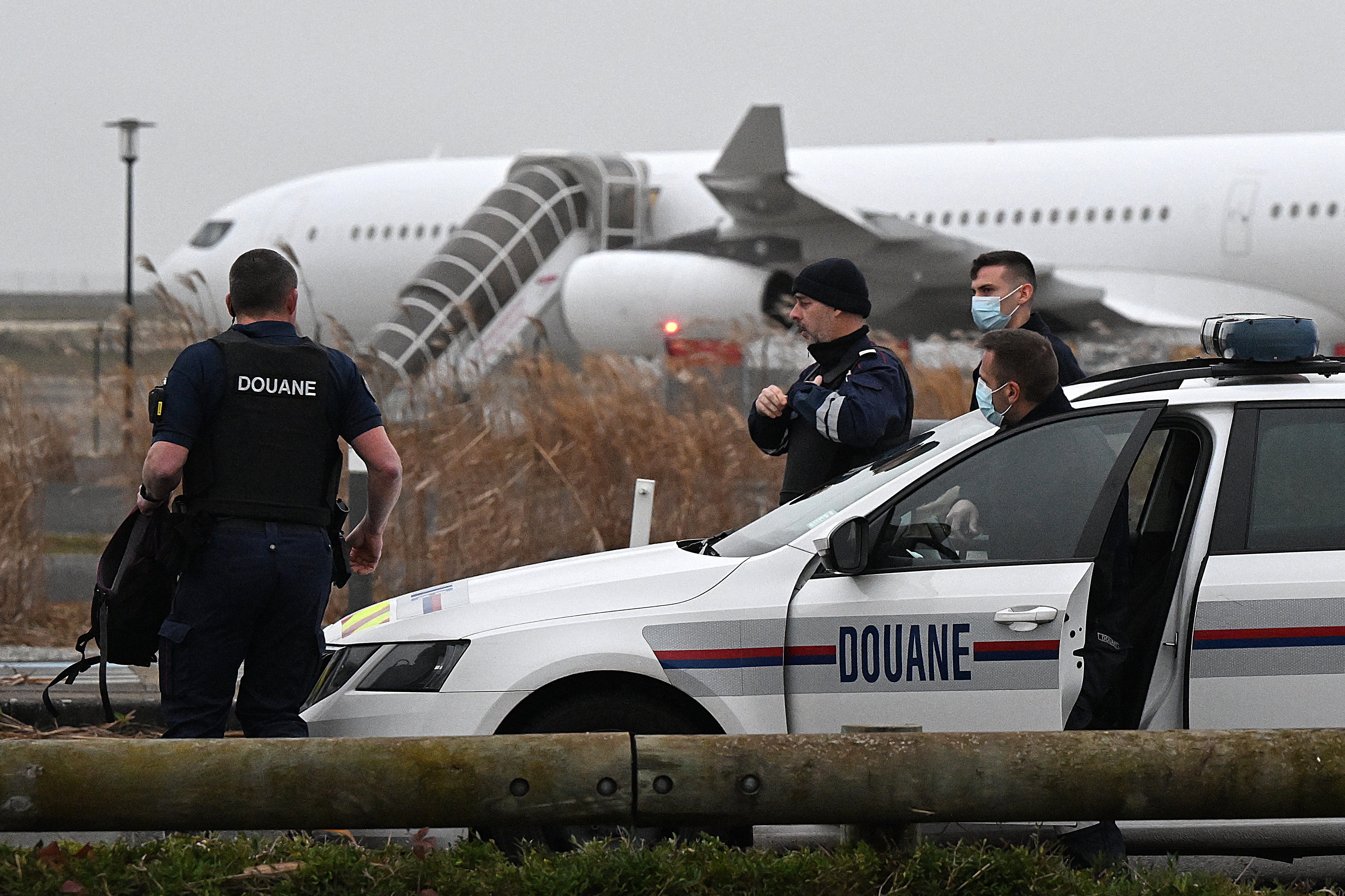 French customs officers stand next to a customs car with an Airbus A340 in the background which was grounded on the tarmac since 21 December over suspected ‘human trafficking’