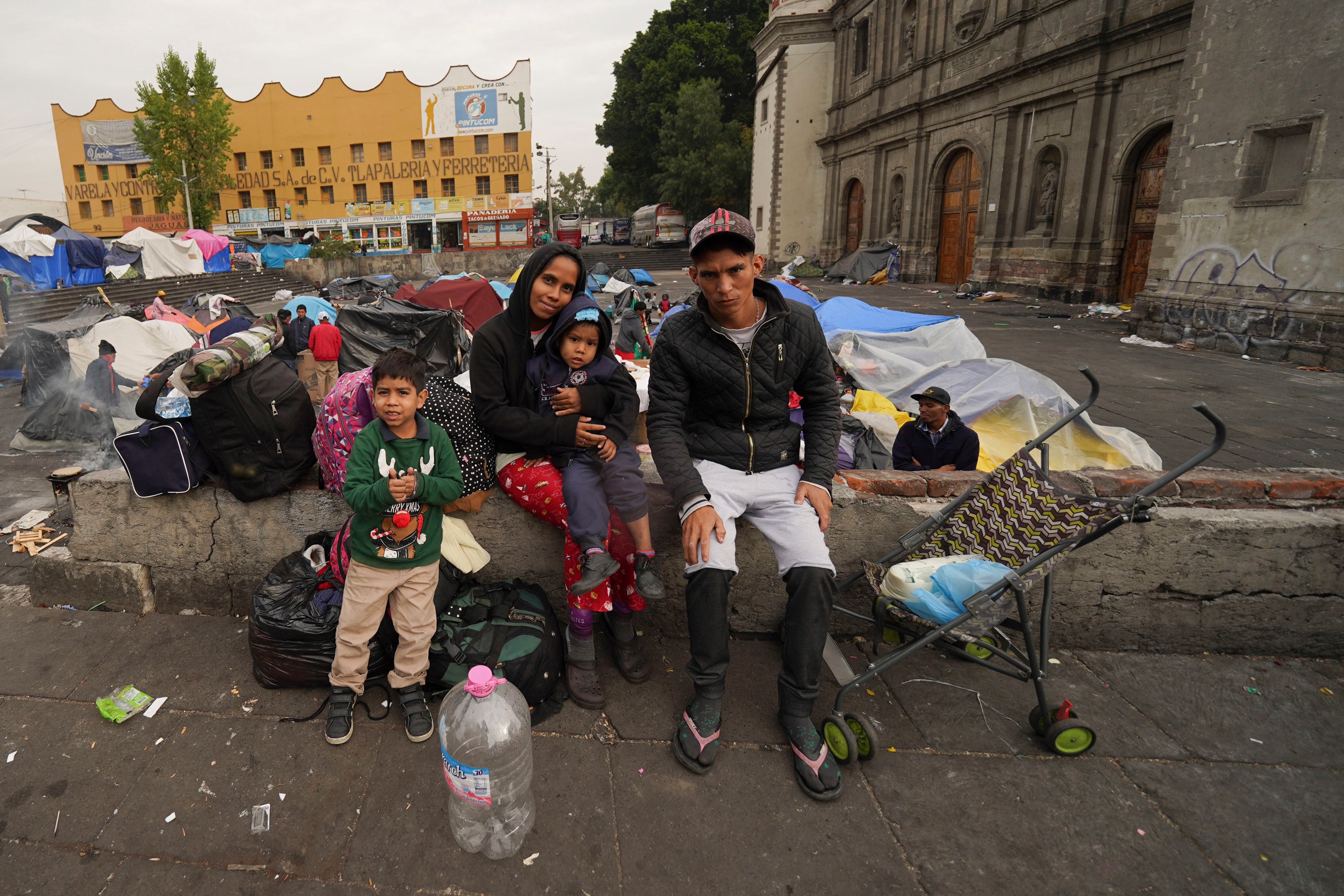 The Aguilar Bastida family, from Venezuela, sit outside the Church of Santa Cruz y La Soledad where migrants camp out i