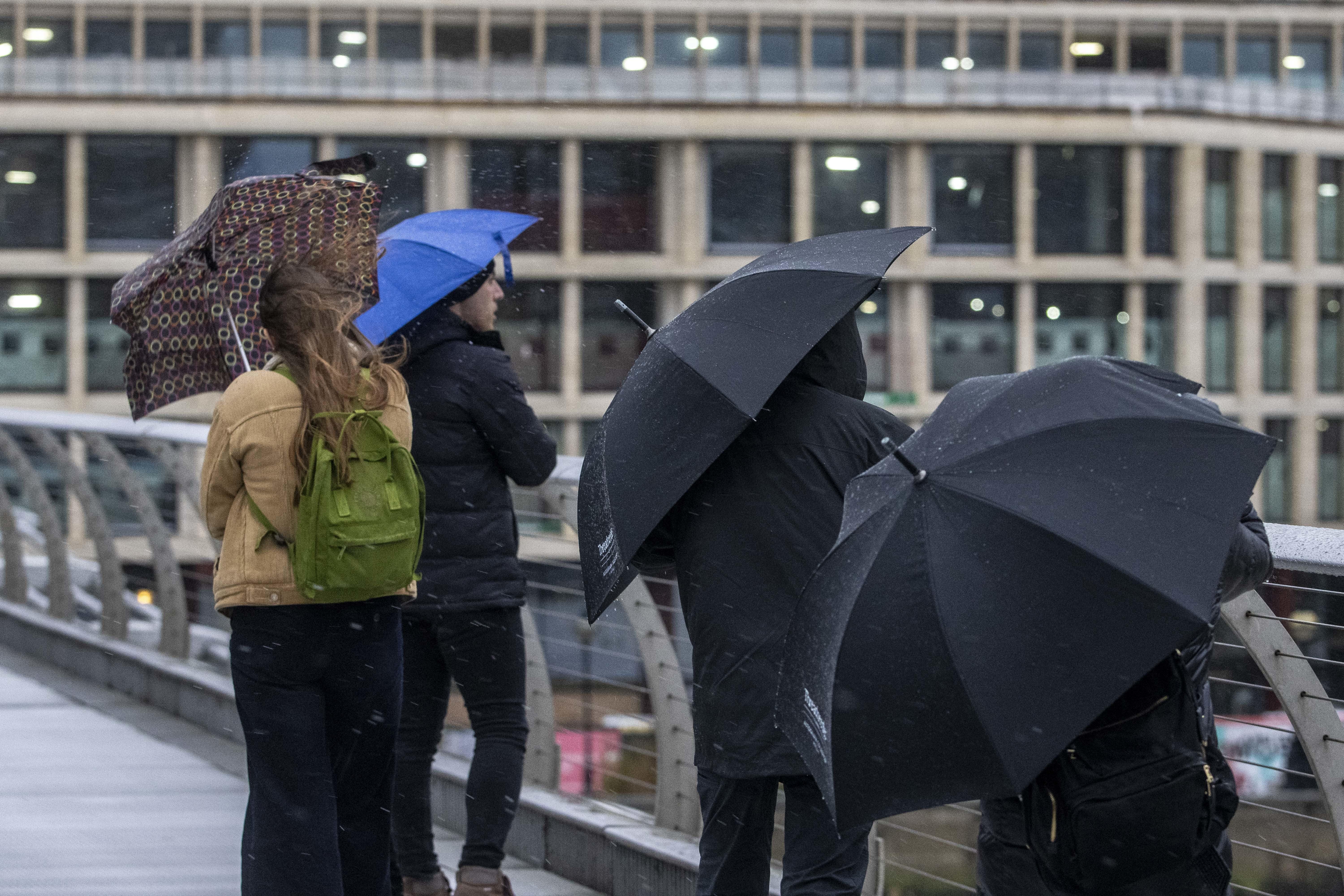 People brave the weather as they cross the Millennium Bridge in London (PA)