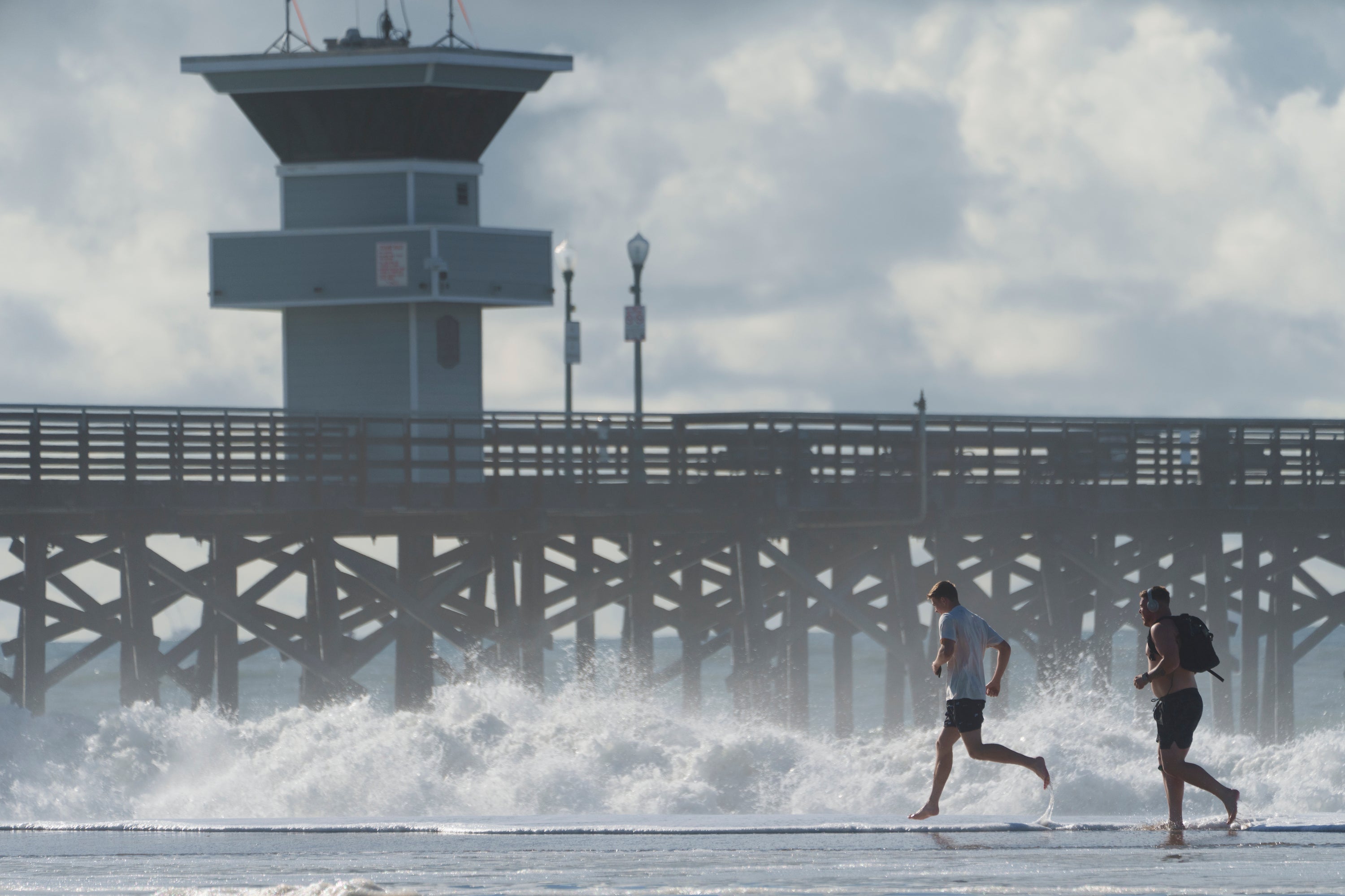 People run on the edge of the flooded beach next to the pier in Seal Beach, California, Saturday, 30 December 2023