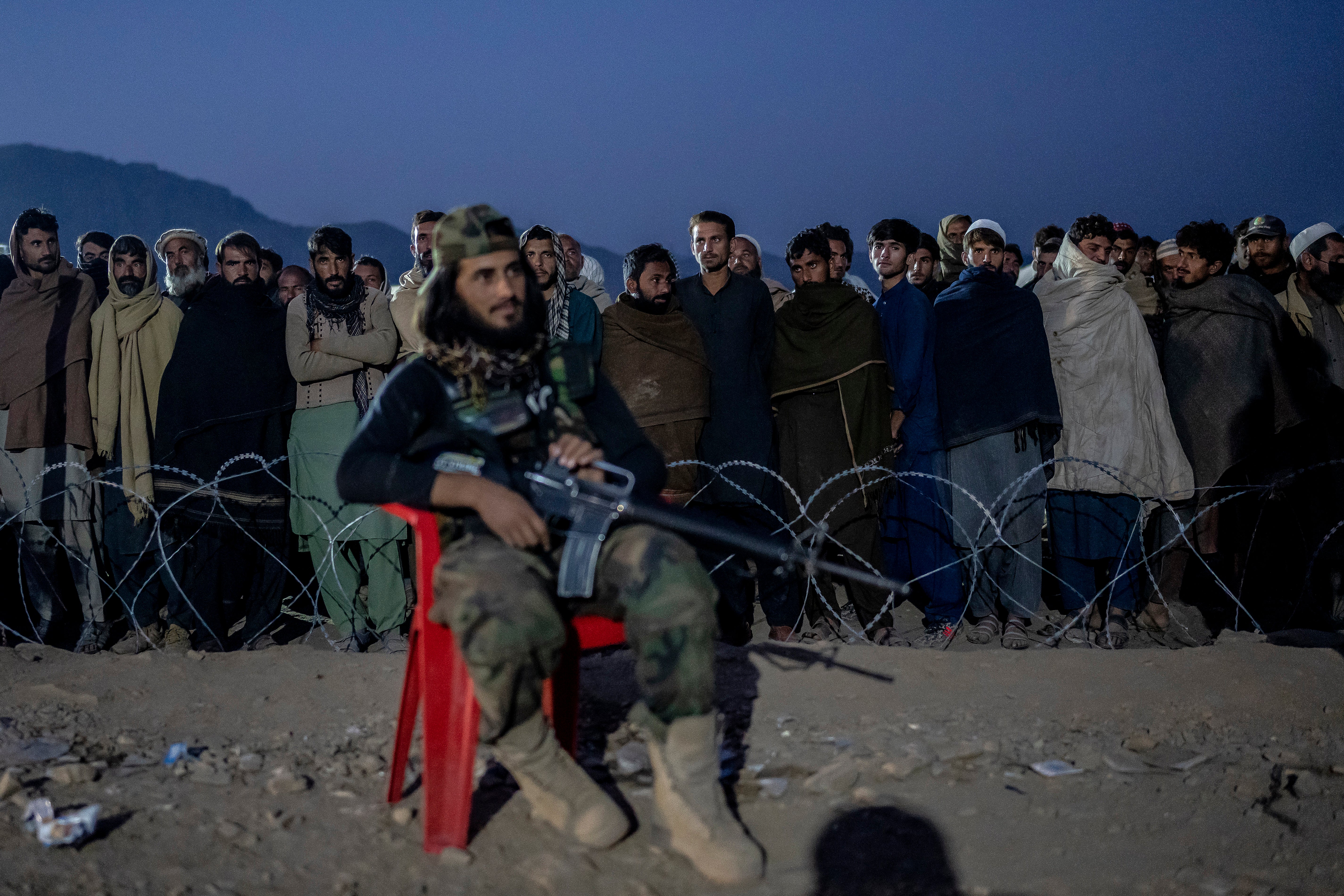 A Taliban fighter stands guard as Afghan refugees line up to register in a camp near the Pakistan-Afghanistan border