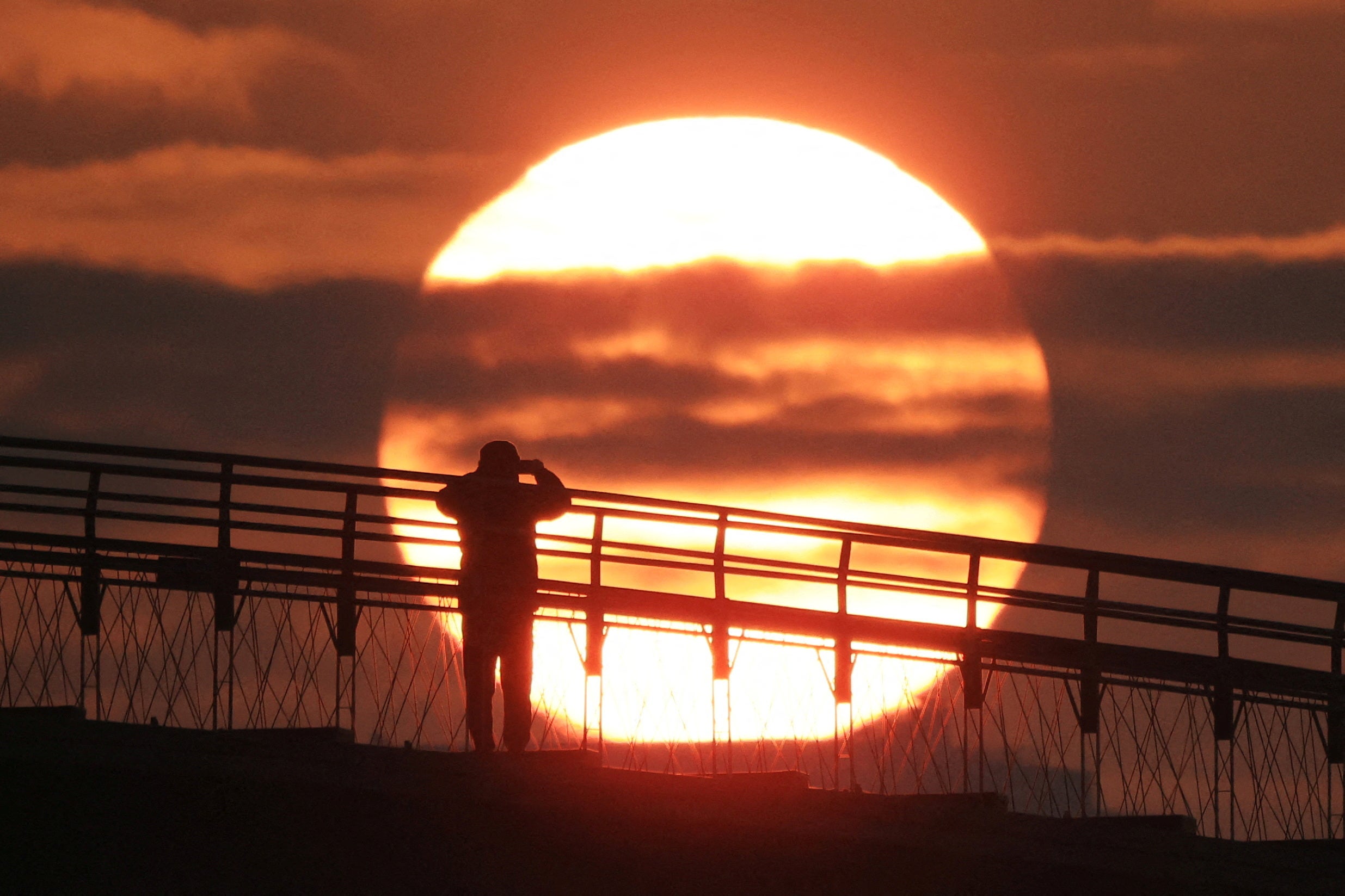 A man on a bridge takes photograph of the first sunrise of the year at a park in Seoul, South Korea, 1 January 2024