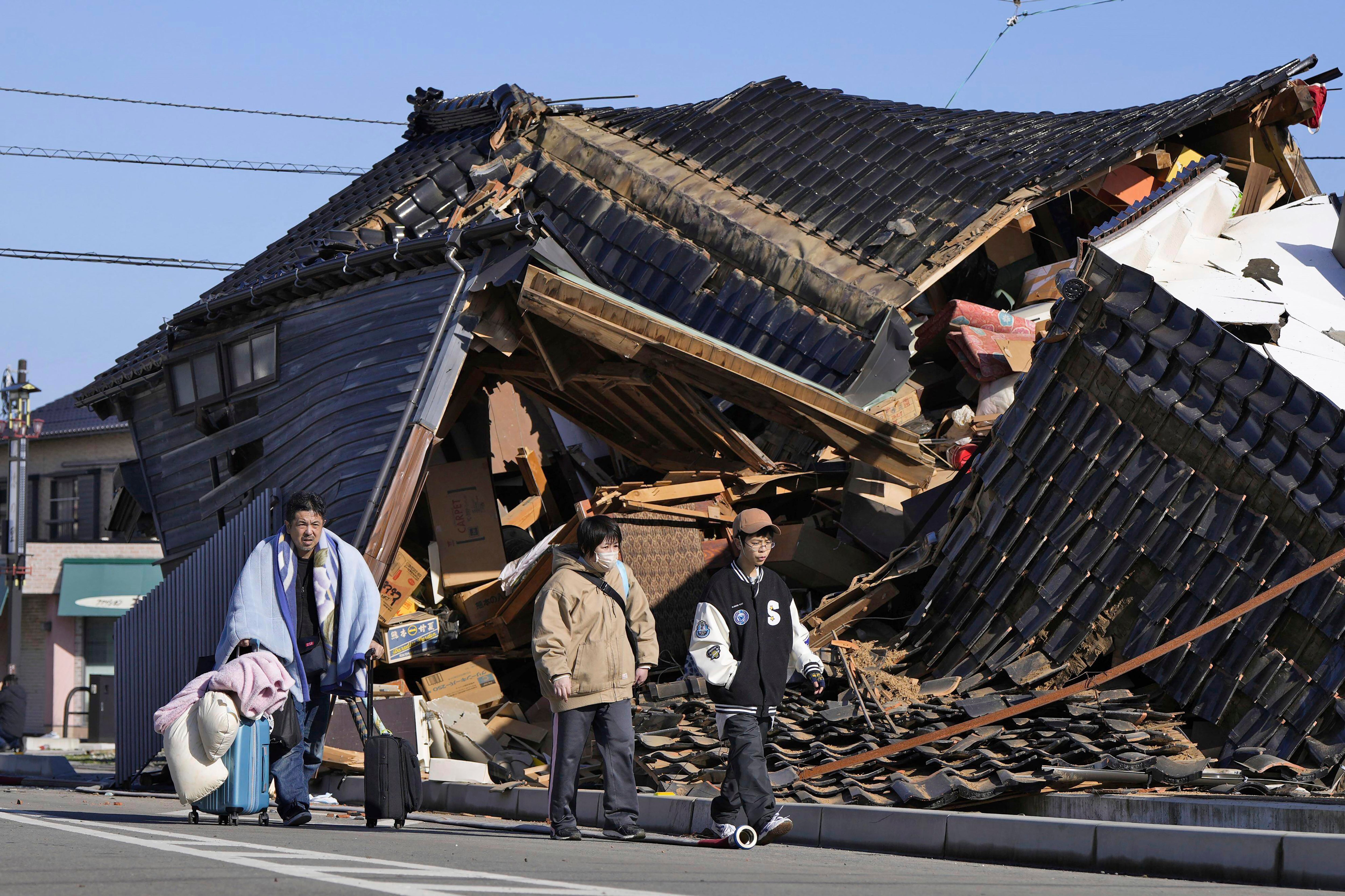 A man carries his belongings past a collapsed house following an earthquake in Wajima, Ishikawa prefecture