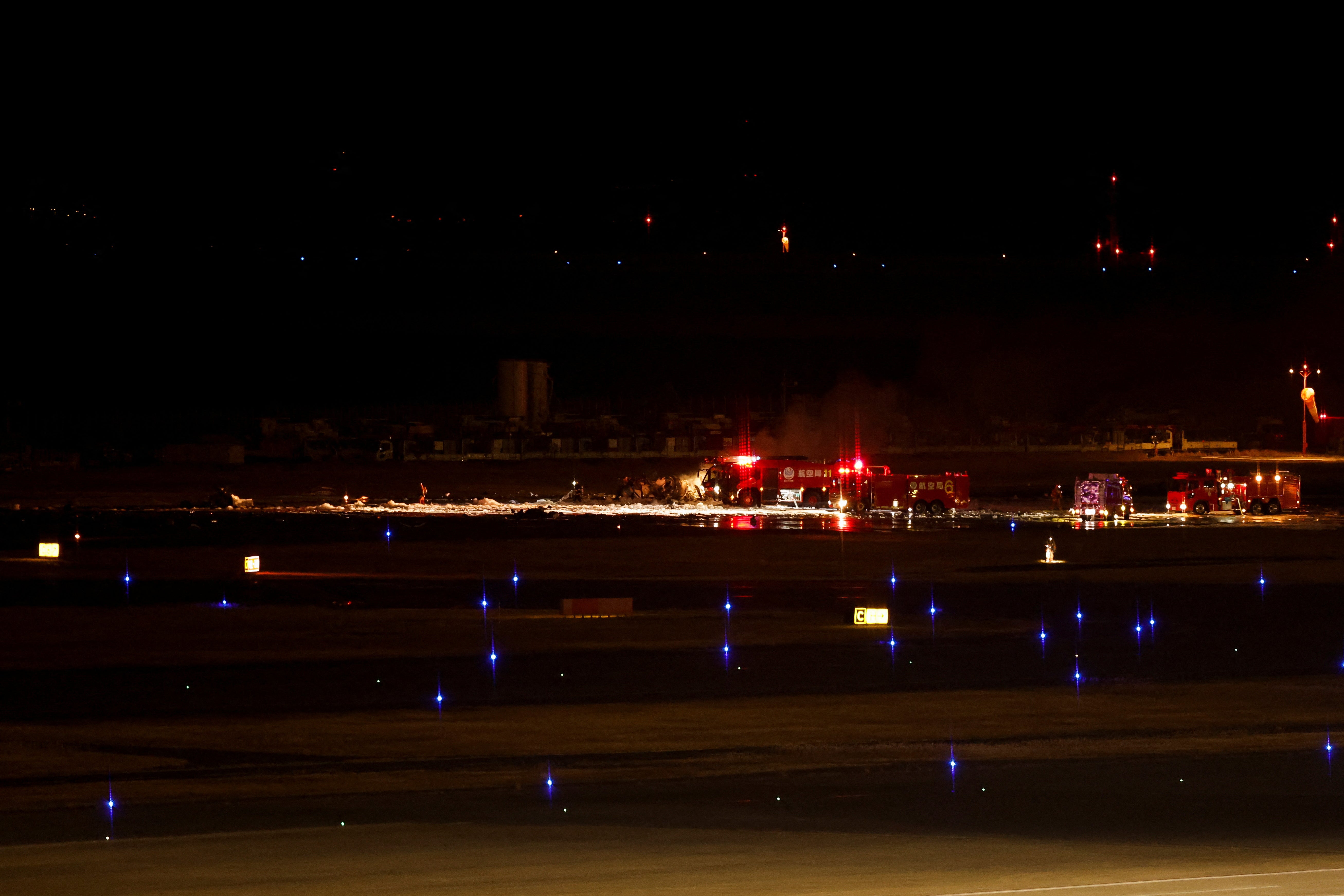 Firefighters work on remnants of a Coast Guard aircraft at Haneda International Airport