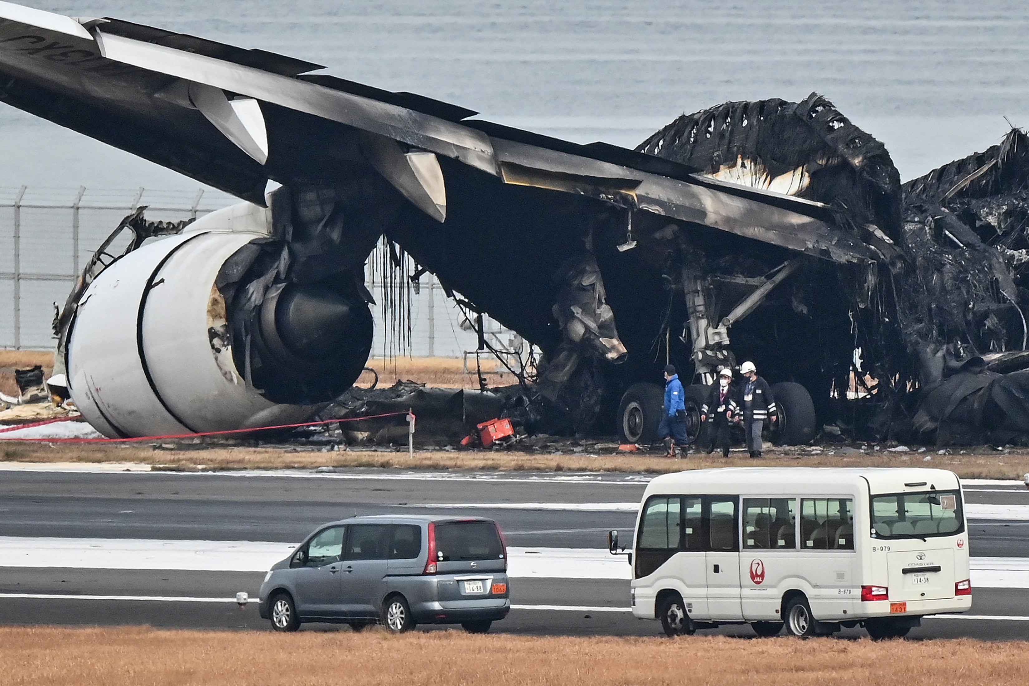 Officials look at the burnt wreckage of a Japan Airlines (JAL) passenger plane on the tarmac at Tokyo International Airport at Haneda