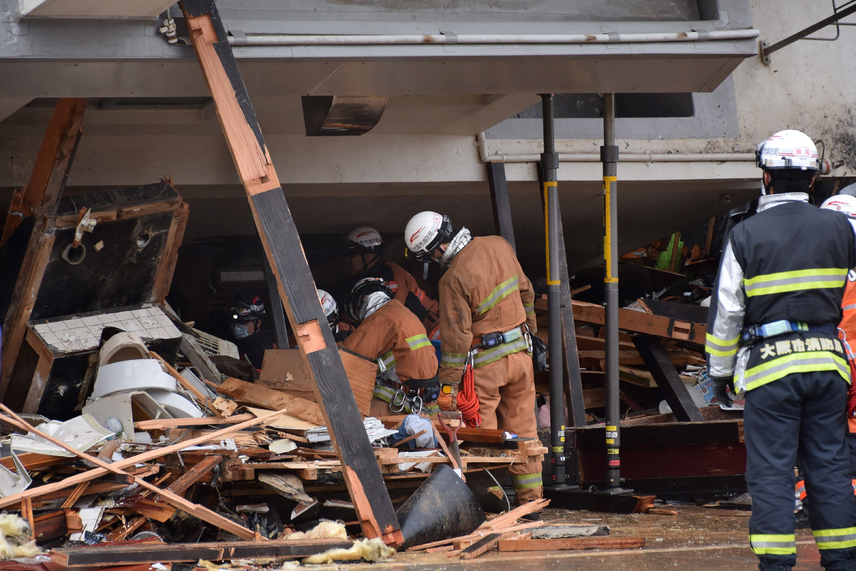 Firefighters work at the scene where a building toppled over and crushed a house in the city of Wajima
