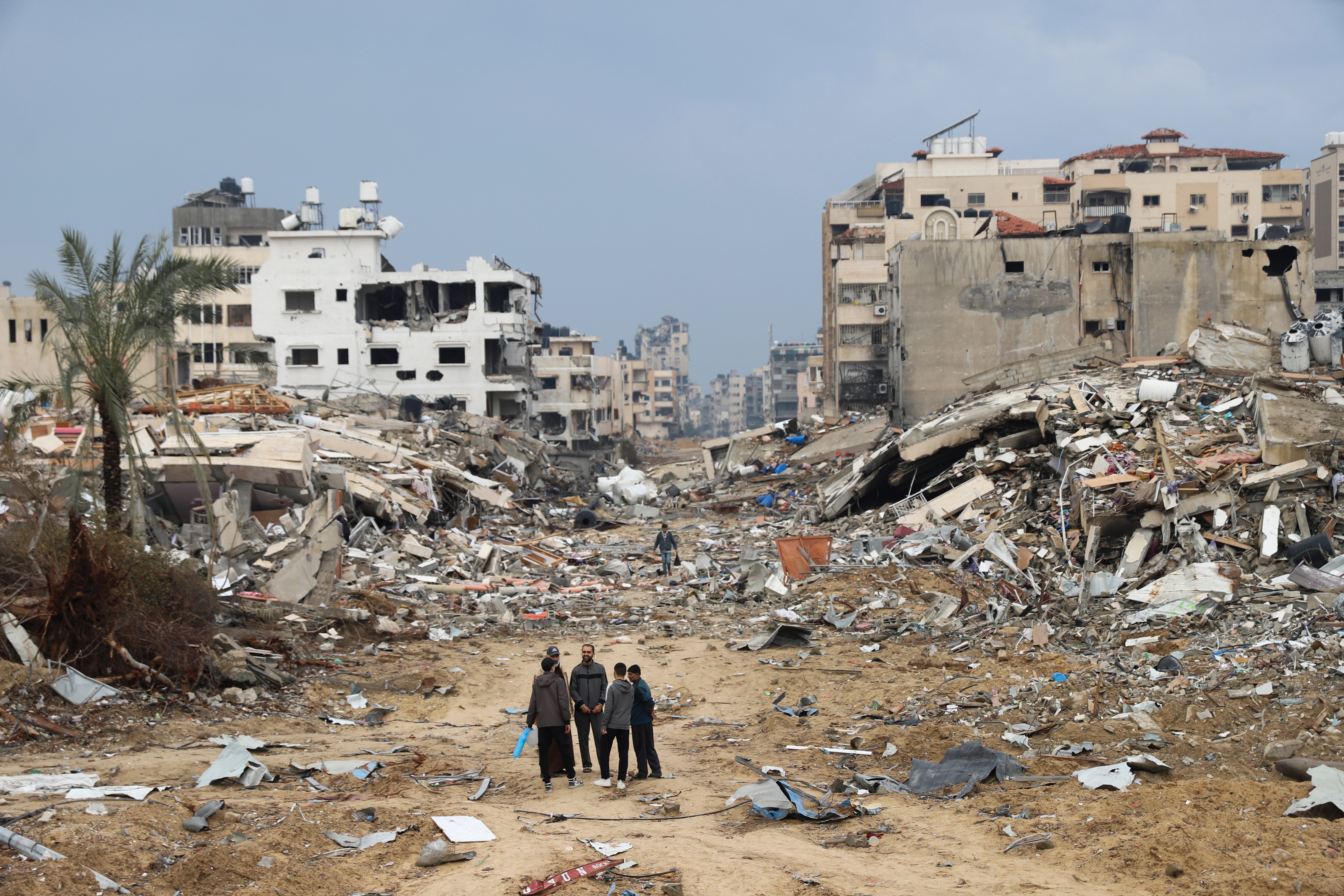 Palestinians in Gaza on 3 January walk past a building destroyed in an Israeli airstrike.