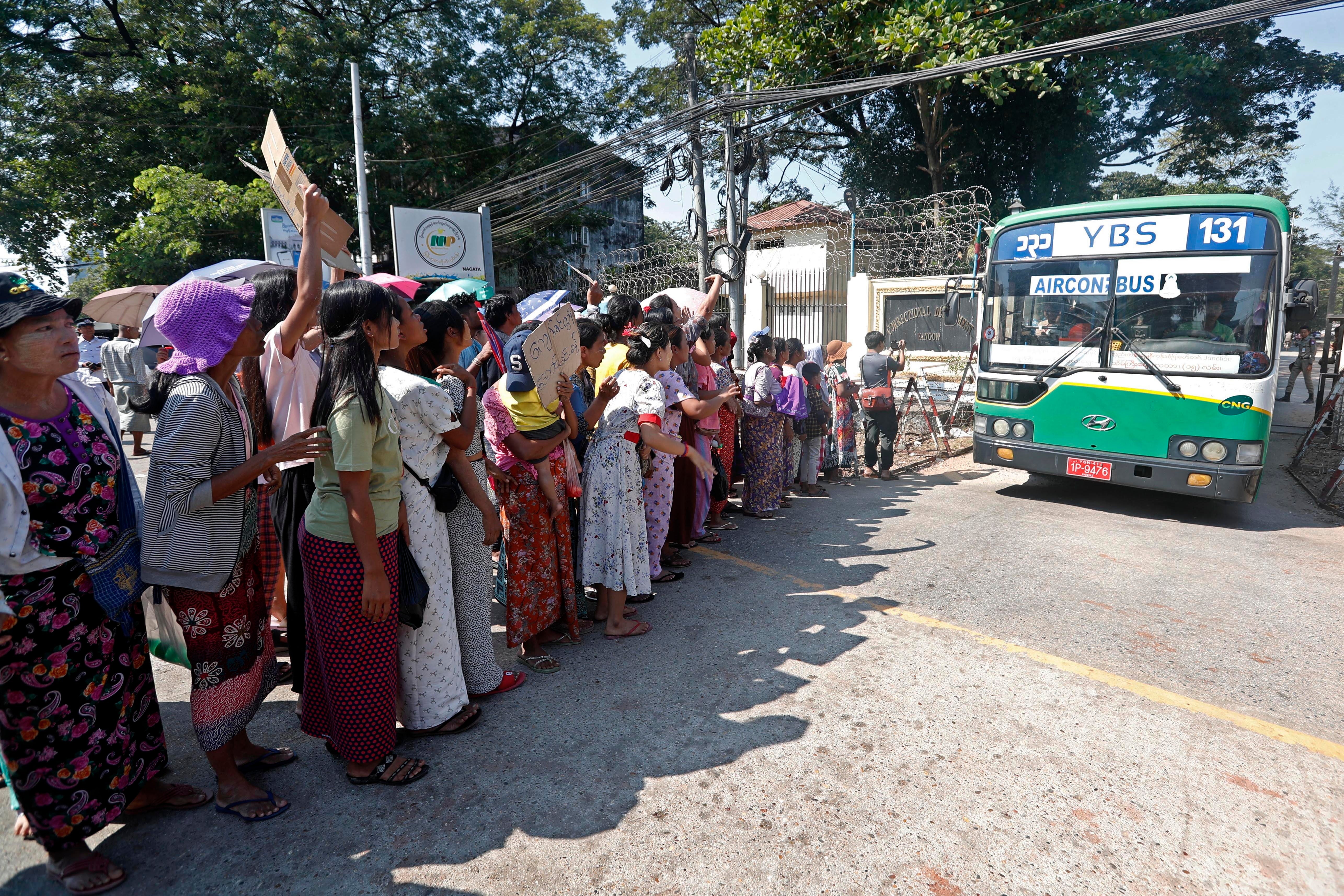 A bus carrying prisoners exits Insein prison as gathered relatives and friends await