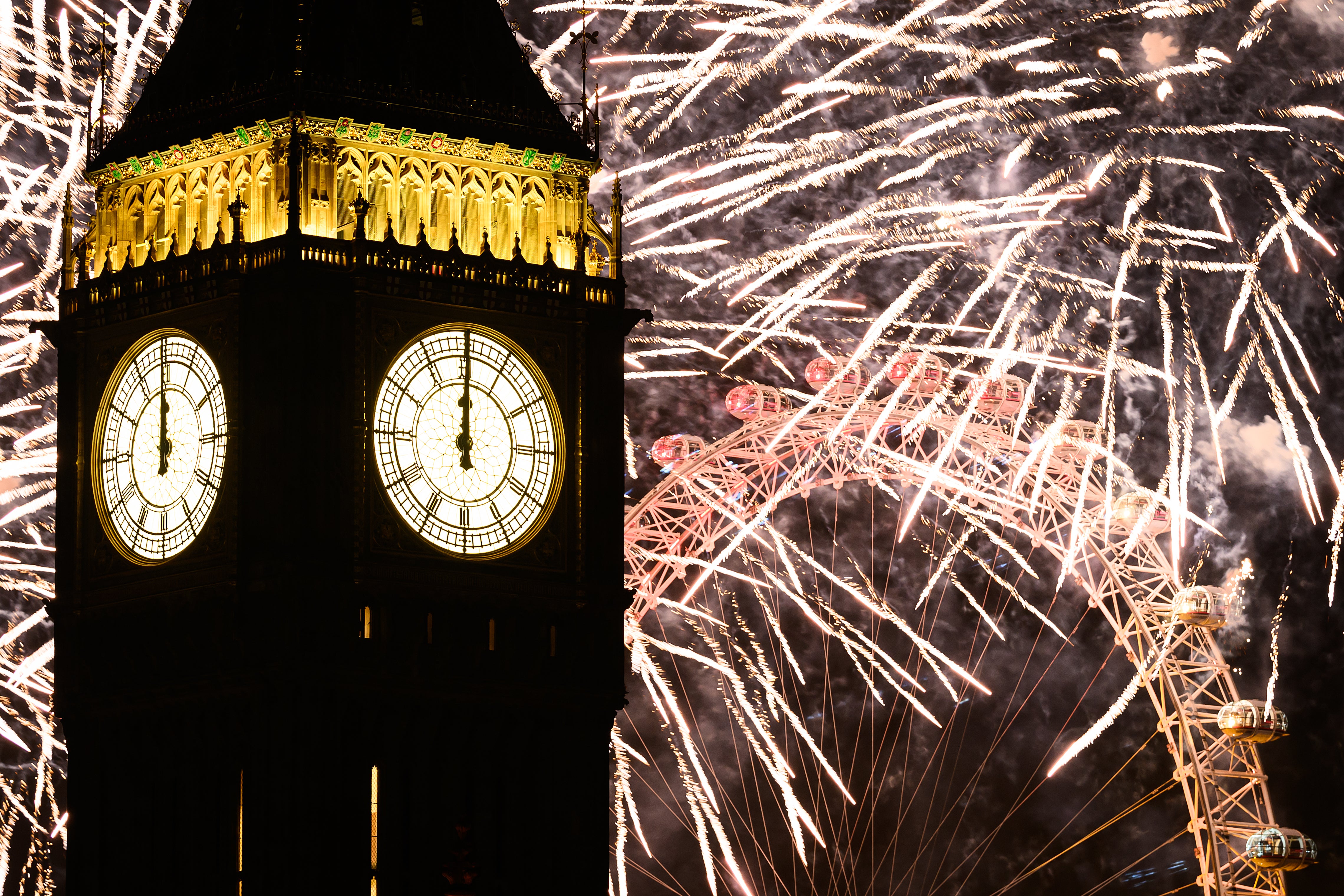 The clock strikes midnight on the face of Queen Elizabeth Tower, commonly known as Big Ben, as fireworks erupt from the London Eye.