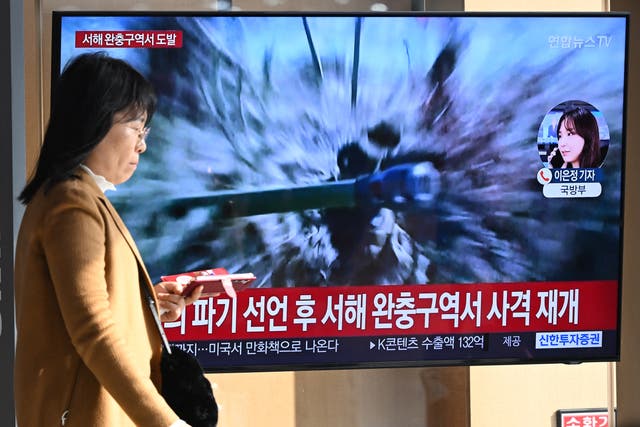 <p>A woman walks past a television screen showing a news broadcast with file footage of North Korea’s artillery firing, at a railway station in Seoul</p>