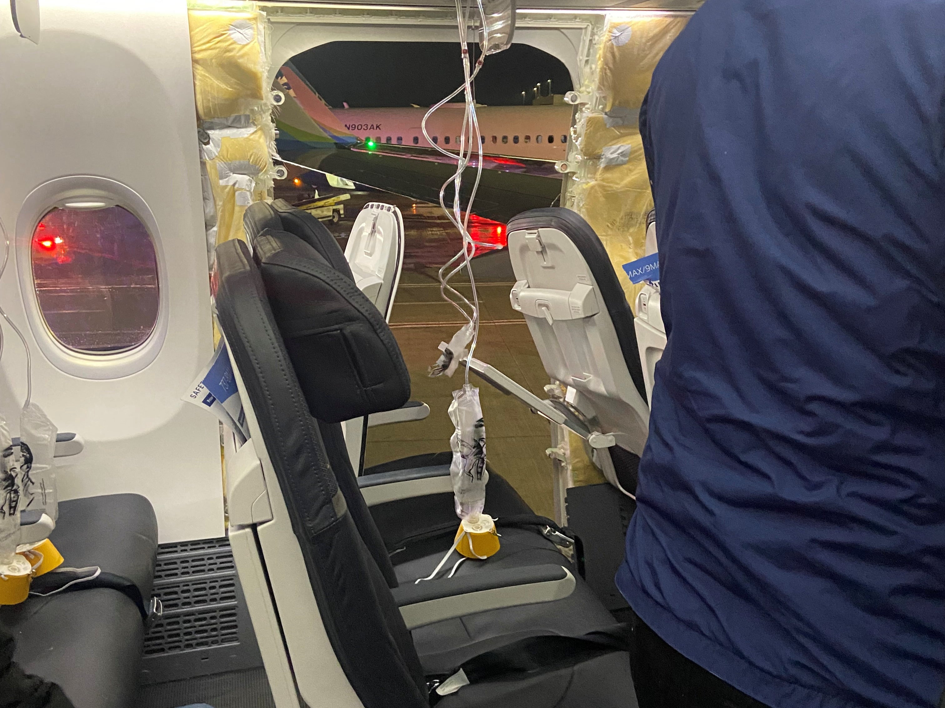 Passenger oxygen masks hang from the roof next to a missing window and a portion of a side wall of an Alaska Airlines Flight 1282