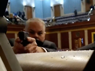 A security guard points his firearm at rioters storming the US Capitol on 6 January 2021 in footage captured on a cellphone