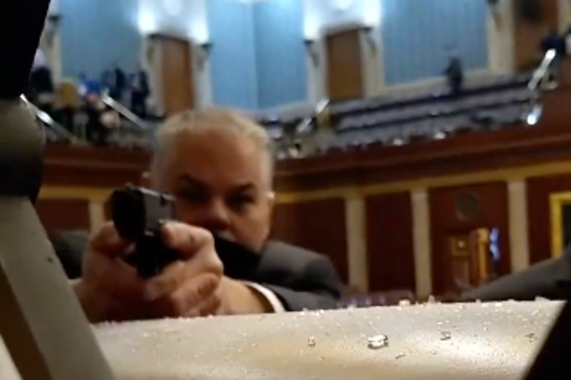 <p>A security guard points his firearm at rioters storming the US Capitol on 6 January 2021 in footage captured on a cellphone</p>