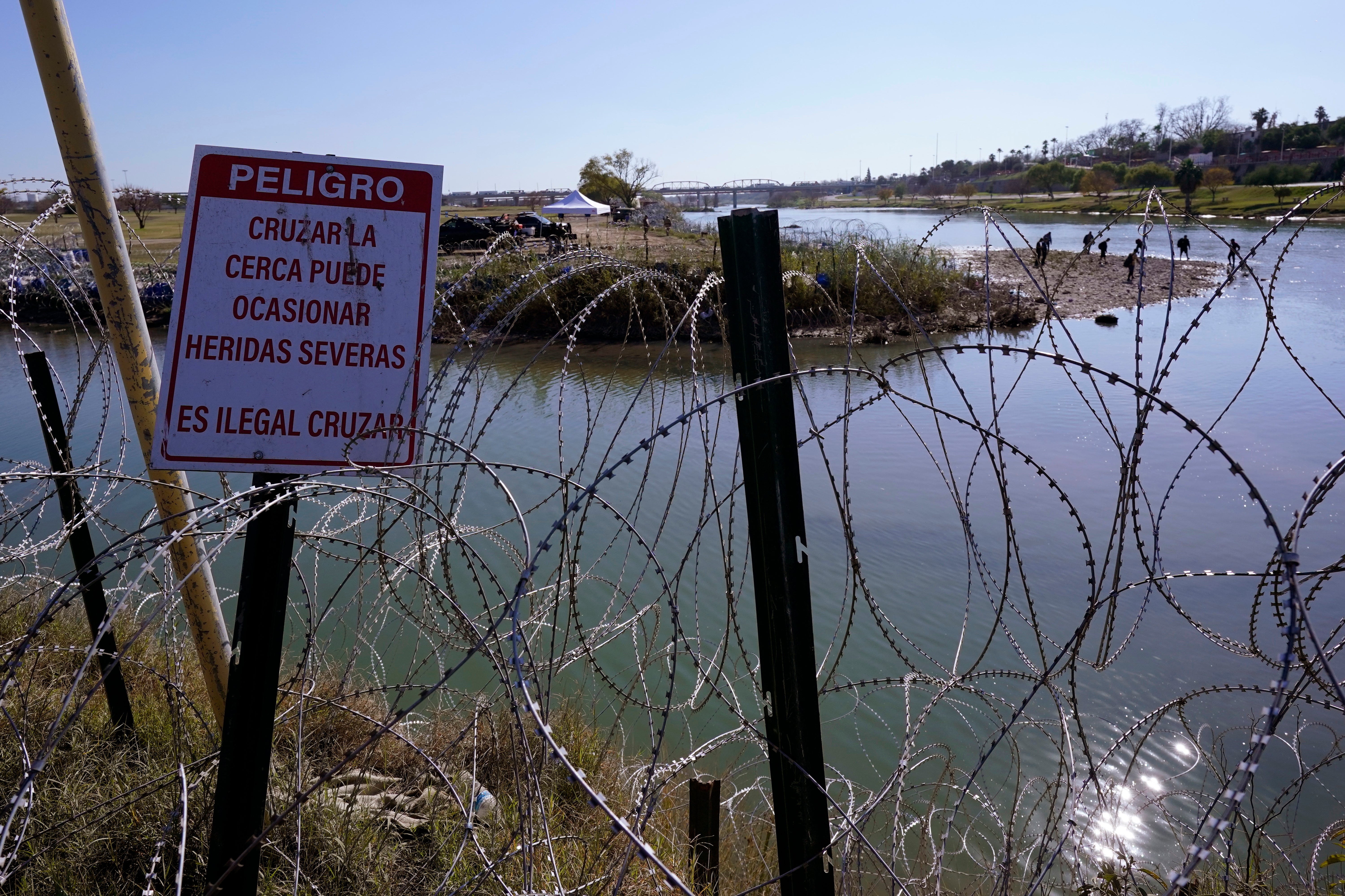 Migrants cross the Rio Grande into the U.S. from Mexico behind Concertina wire and a sign warning that it's dangerous and illegal to cross, Wednesday, Jan. 3, 2024, in Eagle Pass, Texas