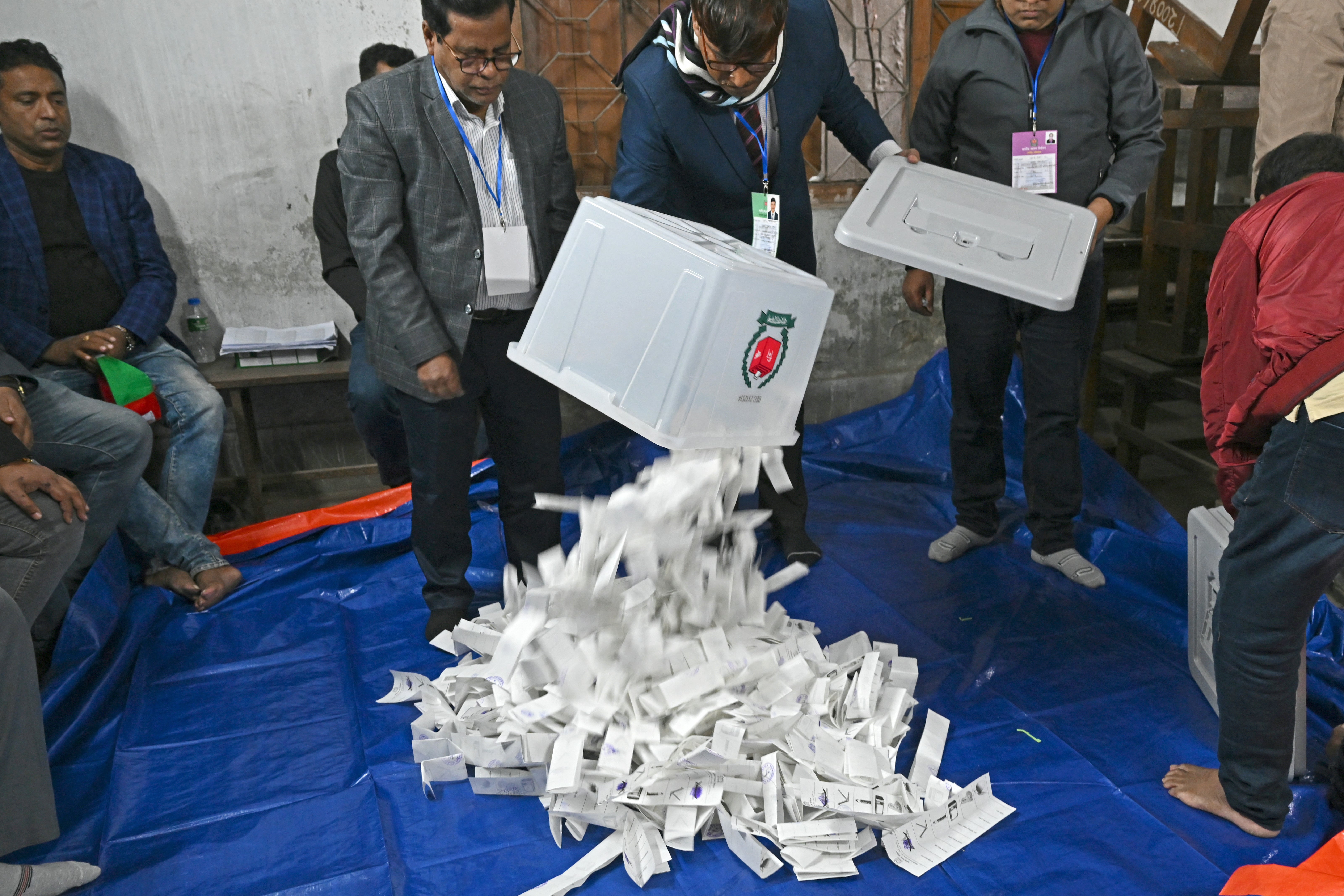Election officials pour ballot papers from a ballot box for counting at a polling booth