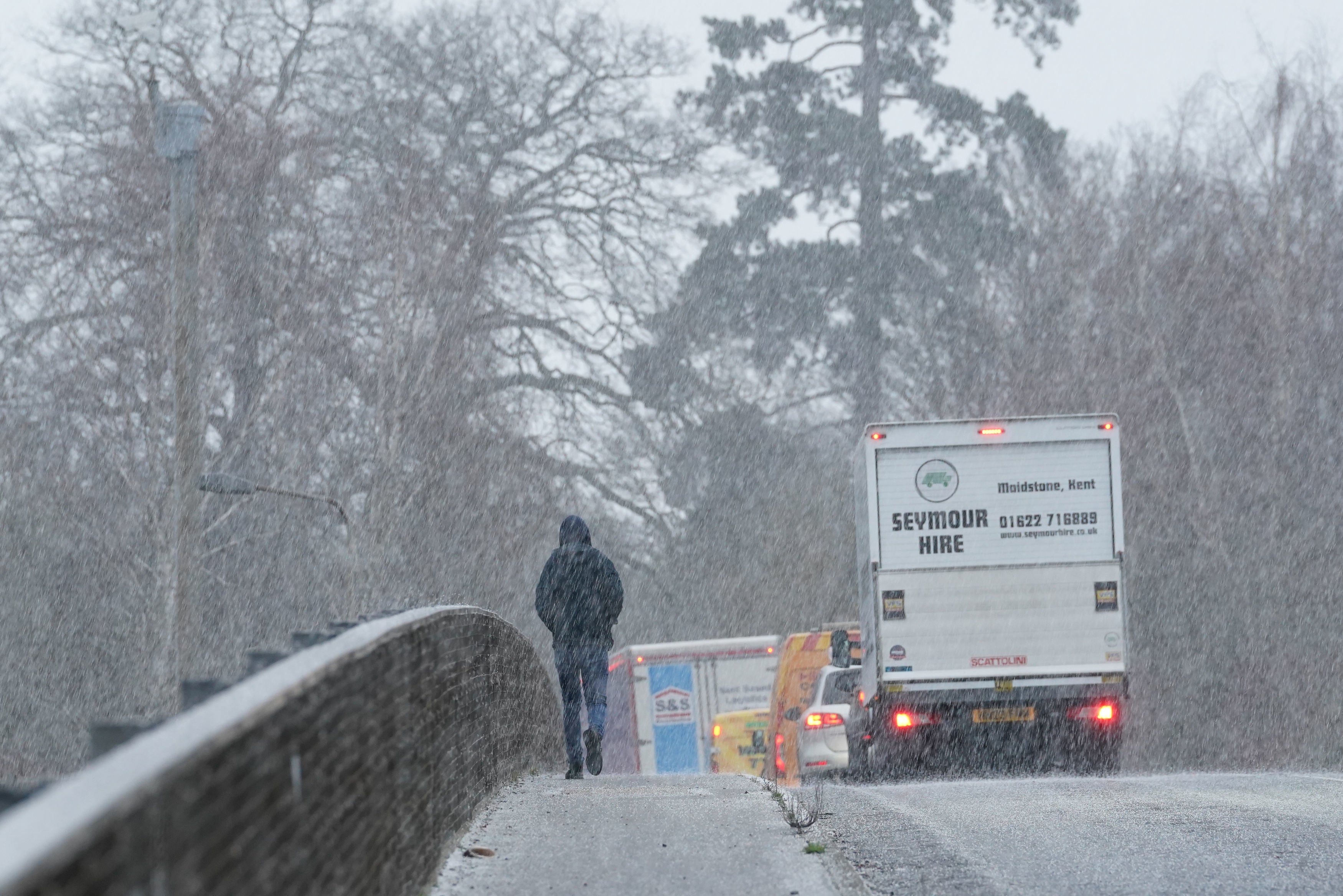 A pedestrian crosses a bridge during a snow shower near Maidstone