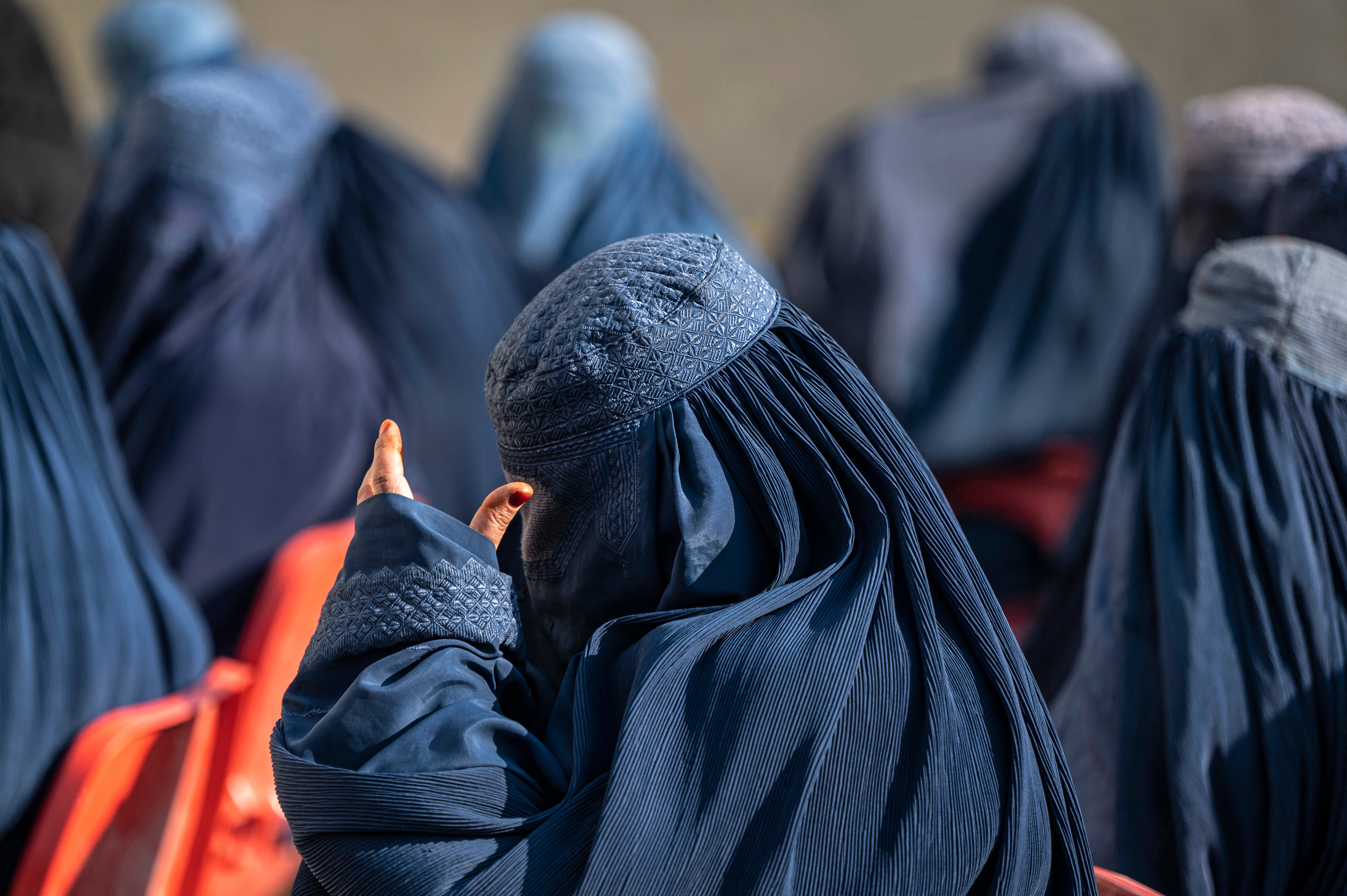 Afghan burqa-clad women sit as they wait to receive cash money in Pul-i-Alam