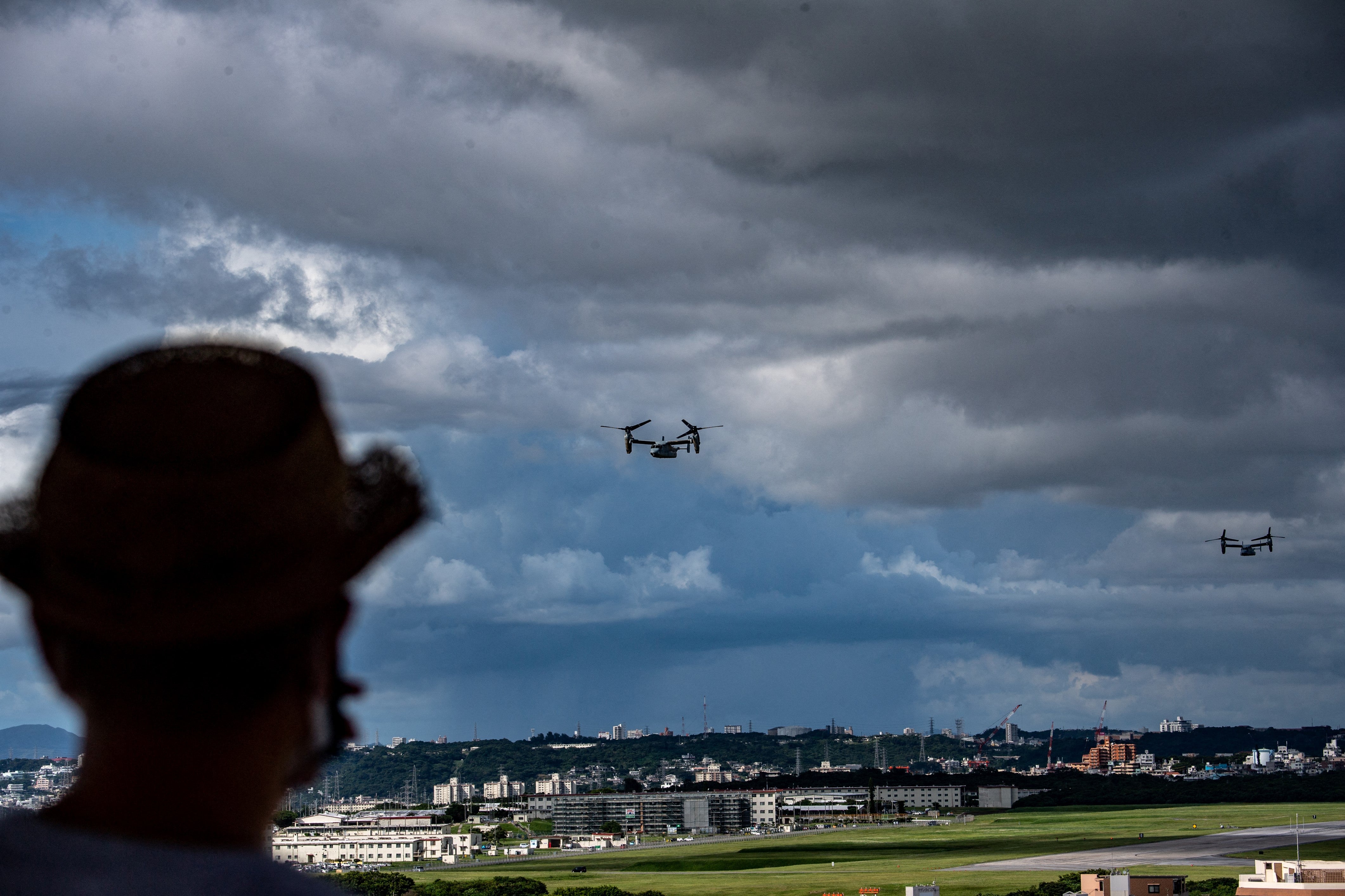 MV-22 Osprey tilt-rotor aircraft in flight after taking off from US Marine Corps Air Station Futenma, as a person looks on towards the military base from Kakazutakadai Park in the city of Ginowan, Okinawa prefecture