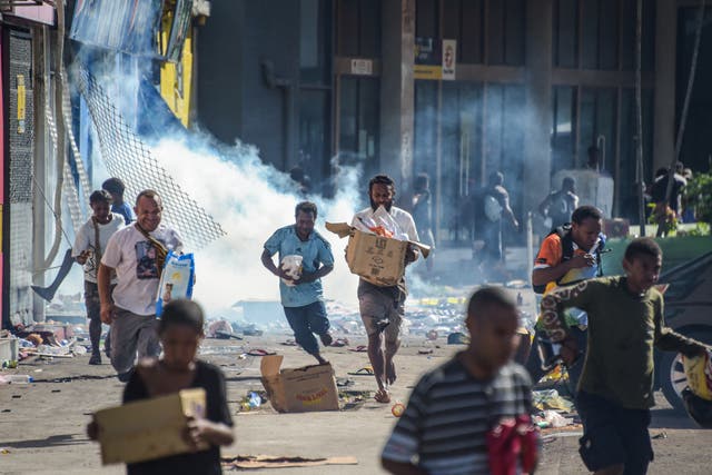 <p>People run with merchandise as crowds leave shops with looted goods amid a state of unrest in Port Moresby on 10 January 2024</p>