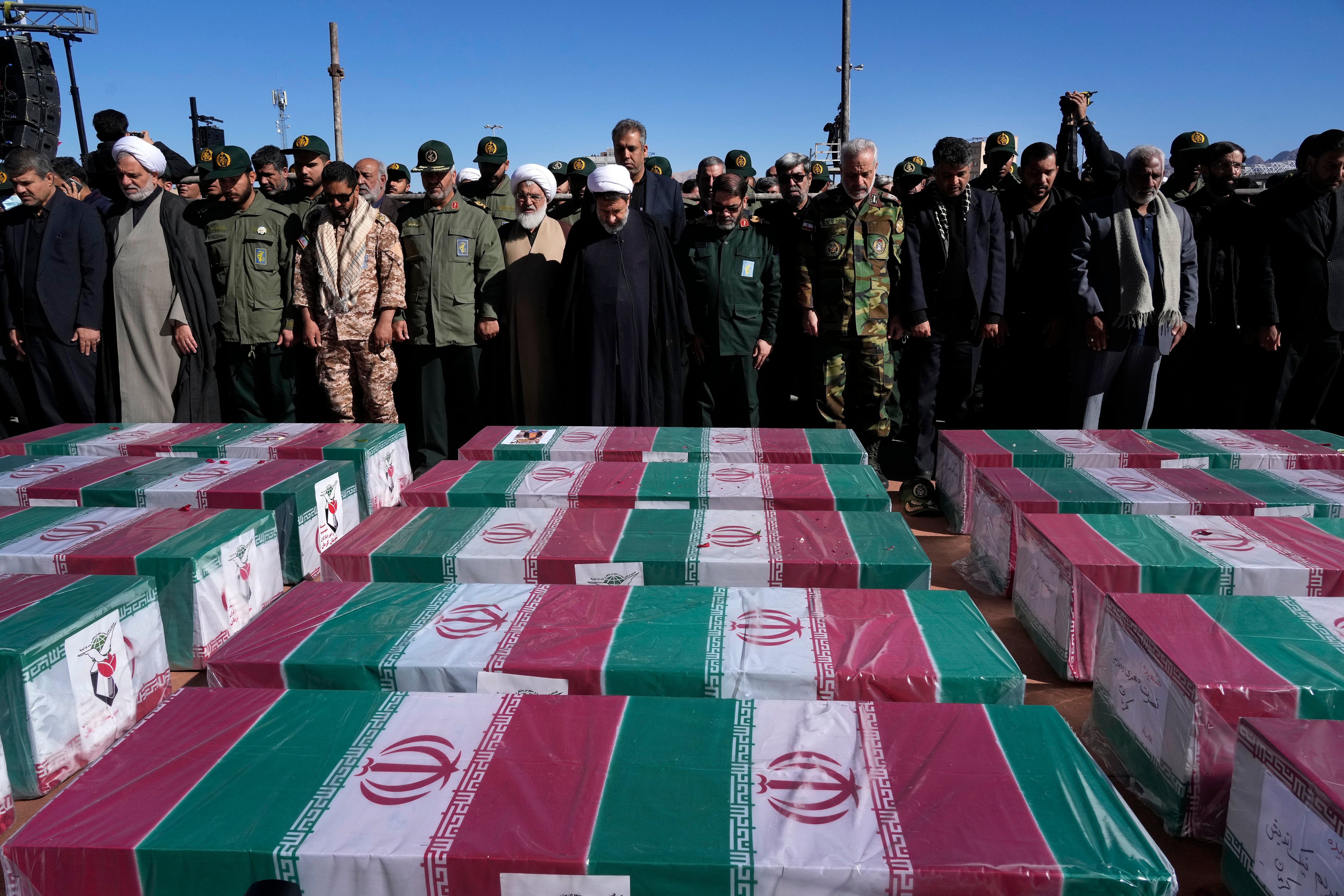 People pray over the flag-draped coffins of victims of the bomb that exploded during a funeral service in the city of Kerman, Iran