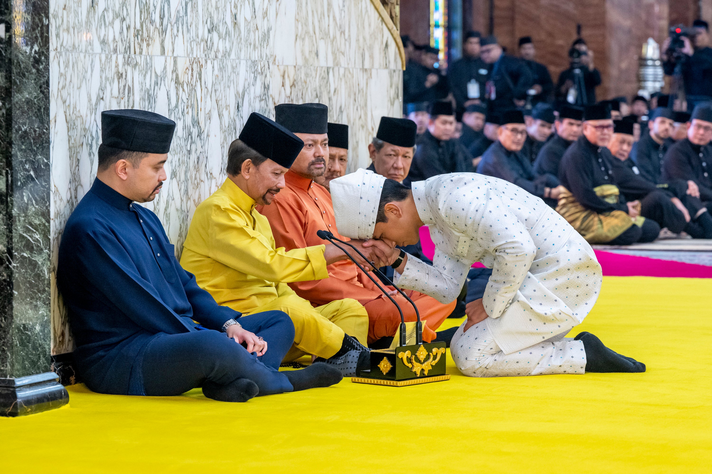 This handout picture taken by Brunei's Information Department on 11 January 2024 and released on 12 January 2024 shows Brunei's Prince Abdul Mateen, right, touching his forehead on his father's hand, Brunei's Sultan Haji Hassanal Bolkiah, second from left, after his solemnisation at Sultan Omar Ali Saifuddien Mosque in Bandar Seri Begawan, Brunei