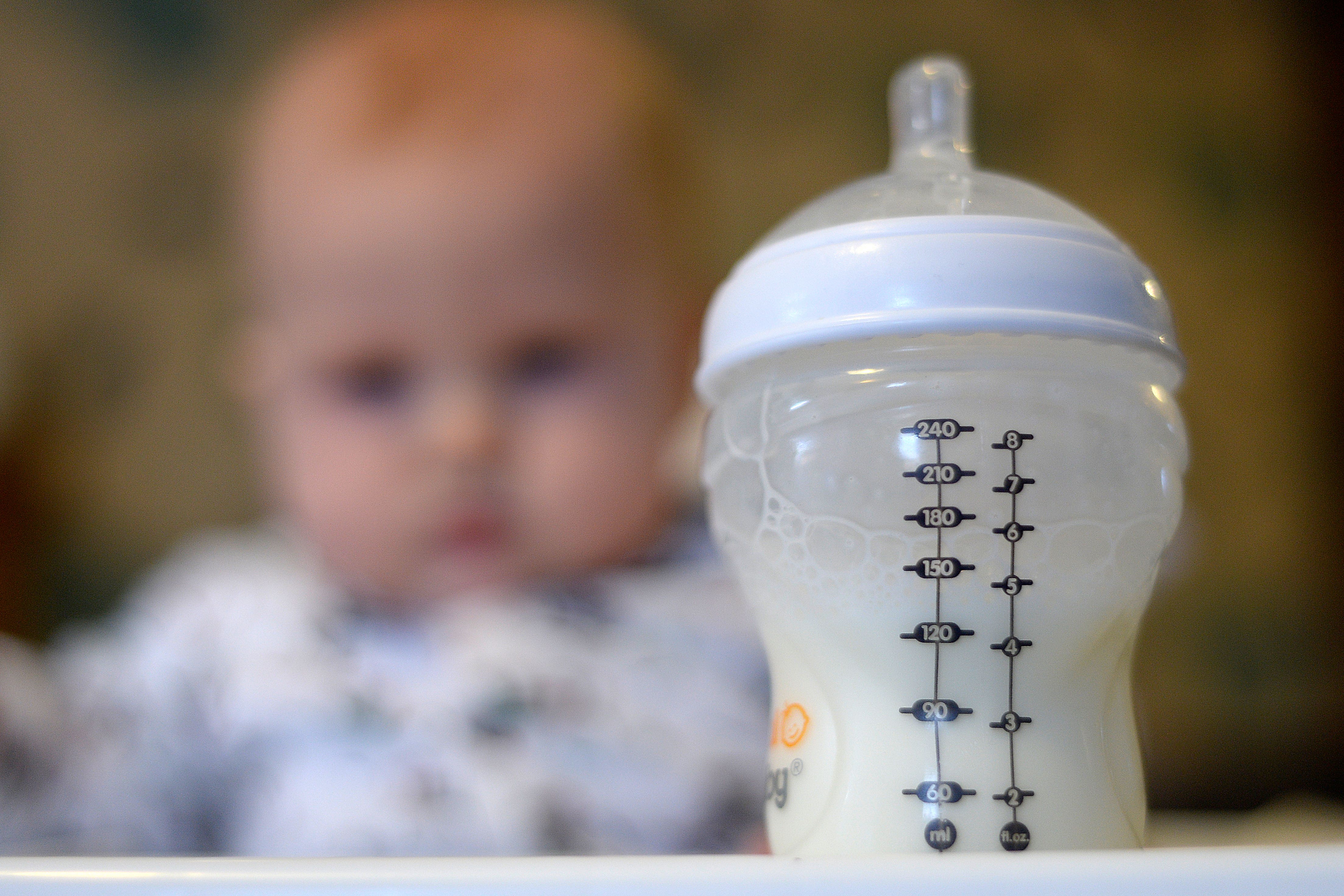 A baby in a high chair looks towards a bottle of milk in the foreground