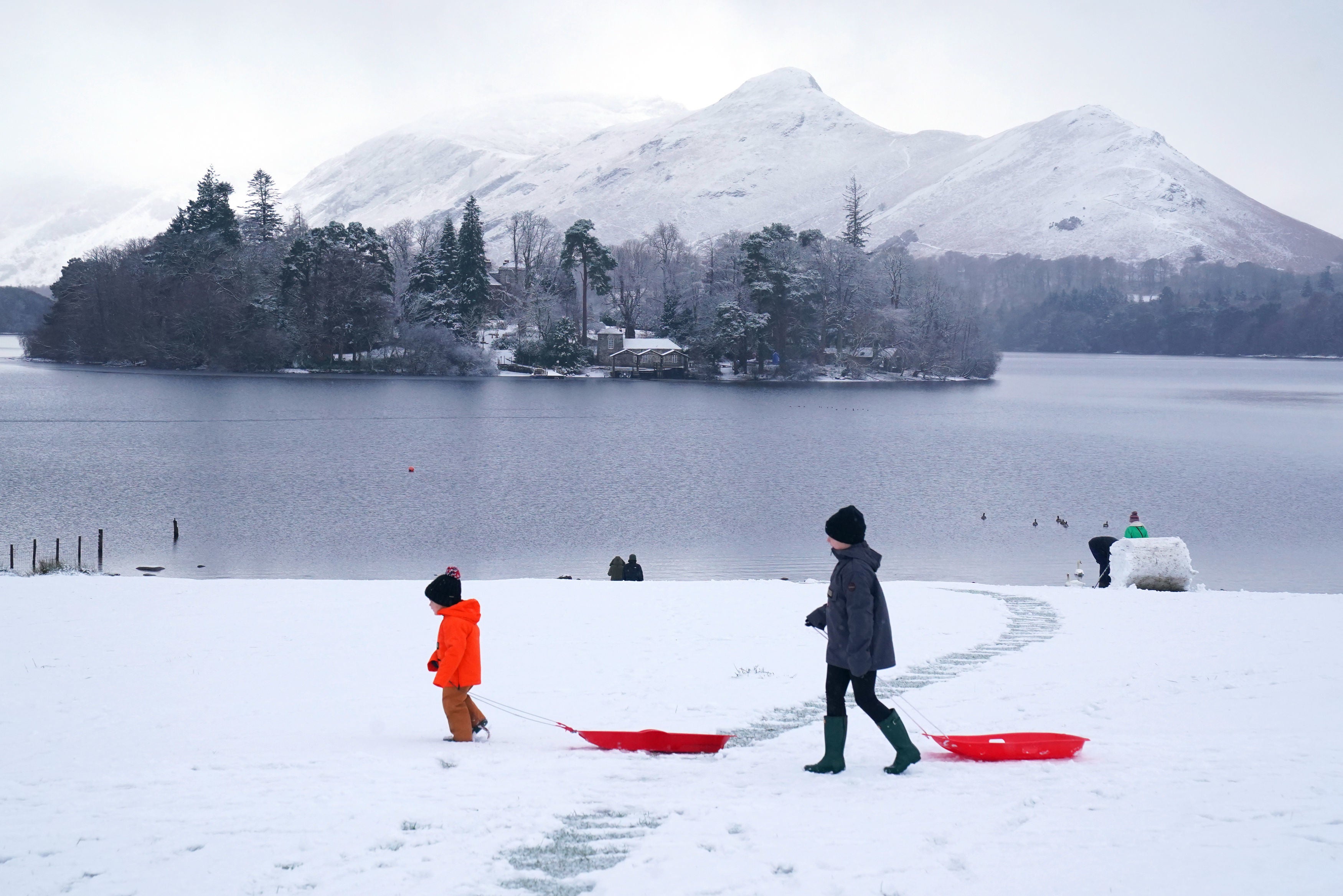 People pulling sledges in snowy conditions in Crow Park at Derwent Water near Keswick, Cumbria