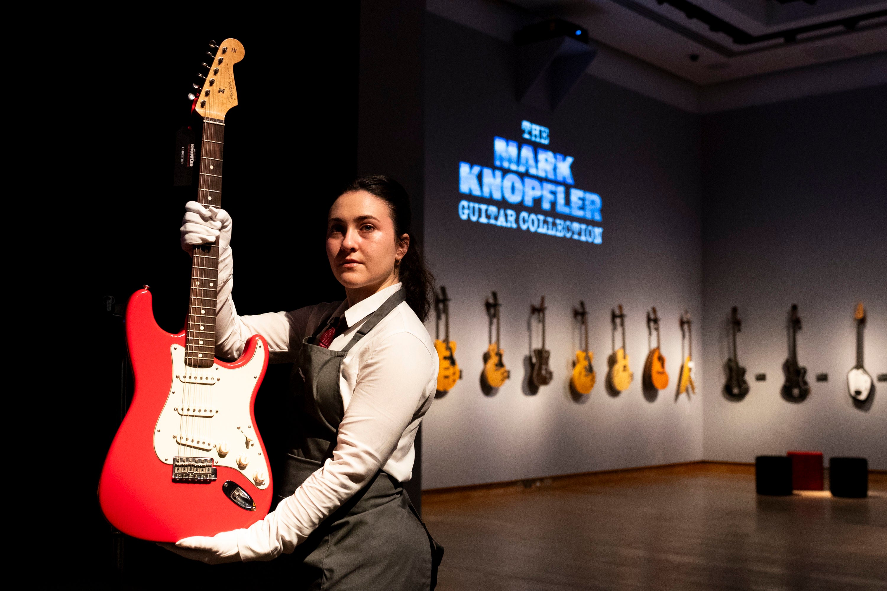 A Christie's art handler holds up Mark Knopfler's Red Schecter Telecaster guitar, among more than 120 guitars to be sold at auction last month