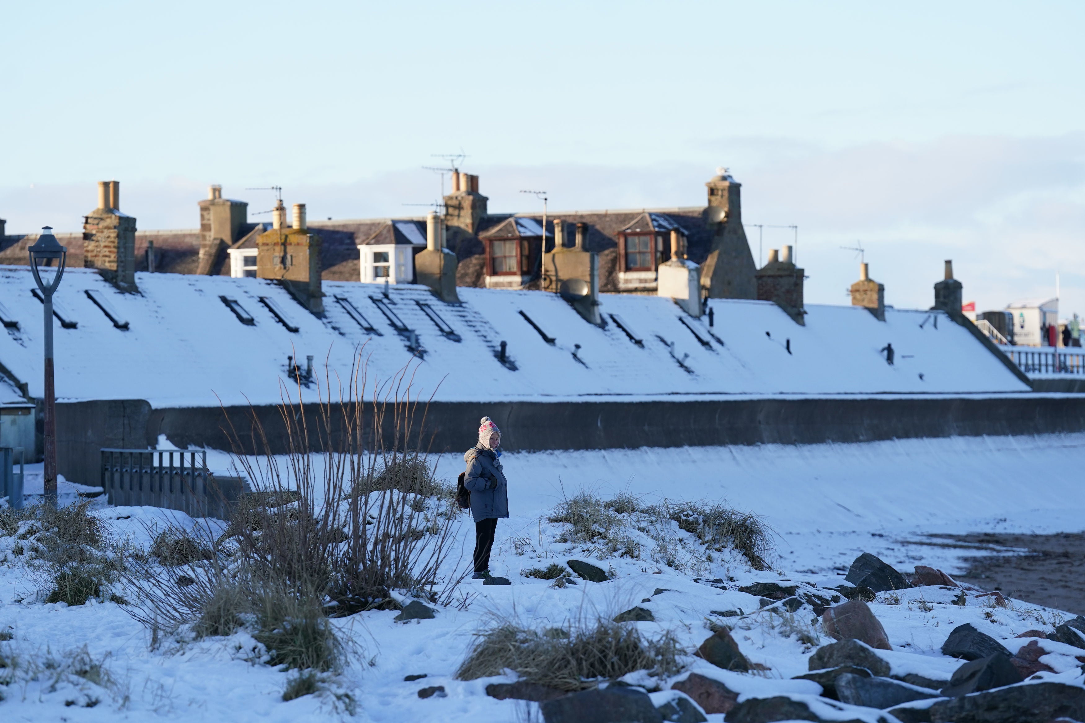 <p>A person looks out from a snow-covered beach front in Aberdeen</p>