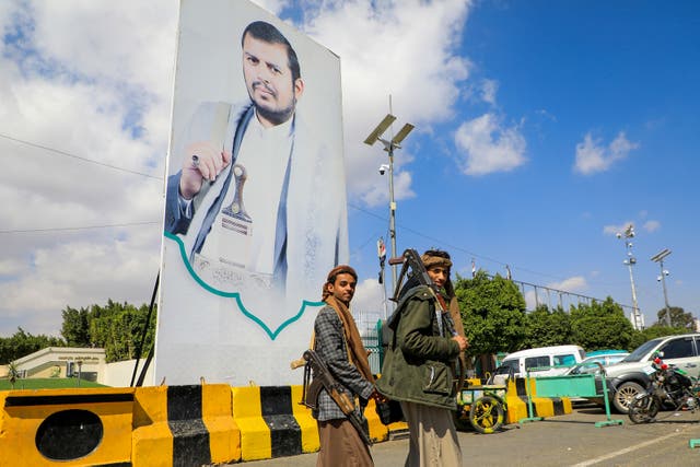 <p>Yemeni fighters walk past a large portrait of Huthi leader Abdulmalik al-Huthi on a street in Sanaa</p>