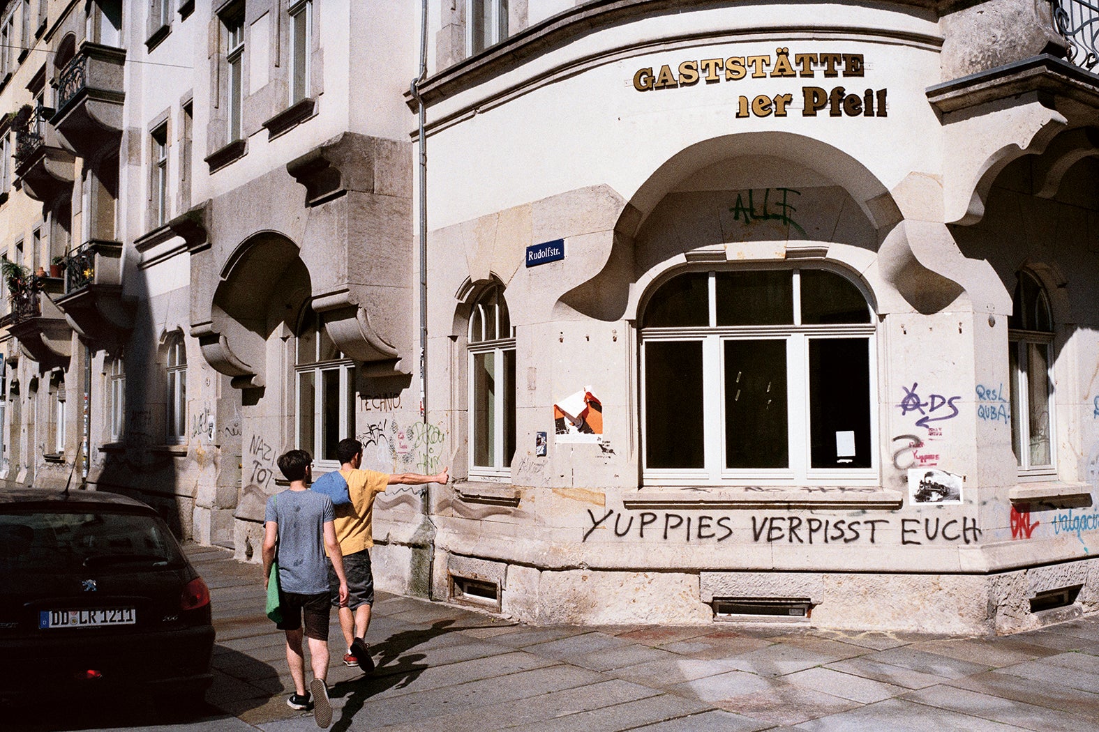 A young man raises his thumb approvingly in the direction of a graffiti reading ‘Yuppies f*** off’ on the wall of a closed restaurant in Dresden