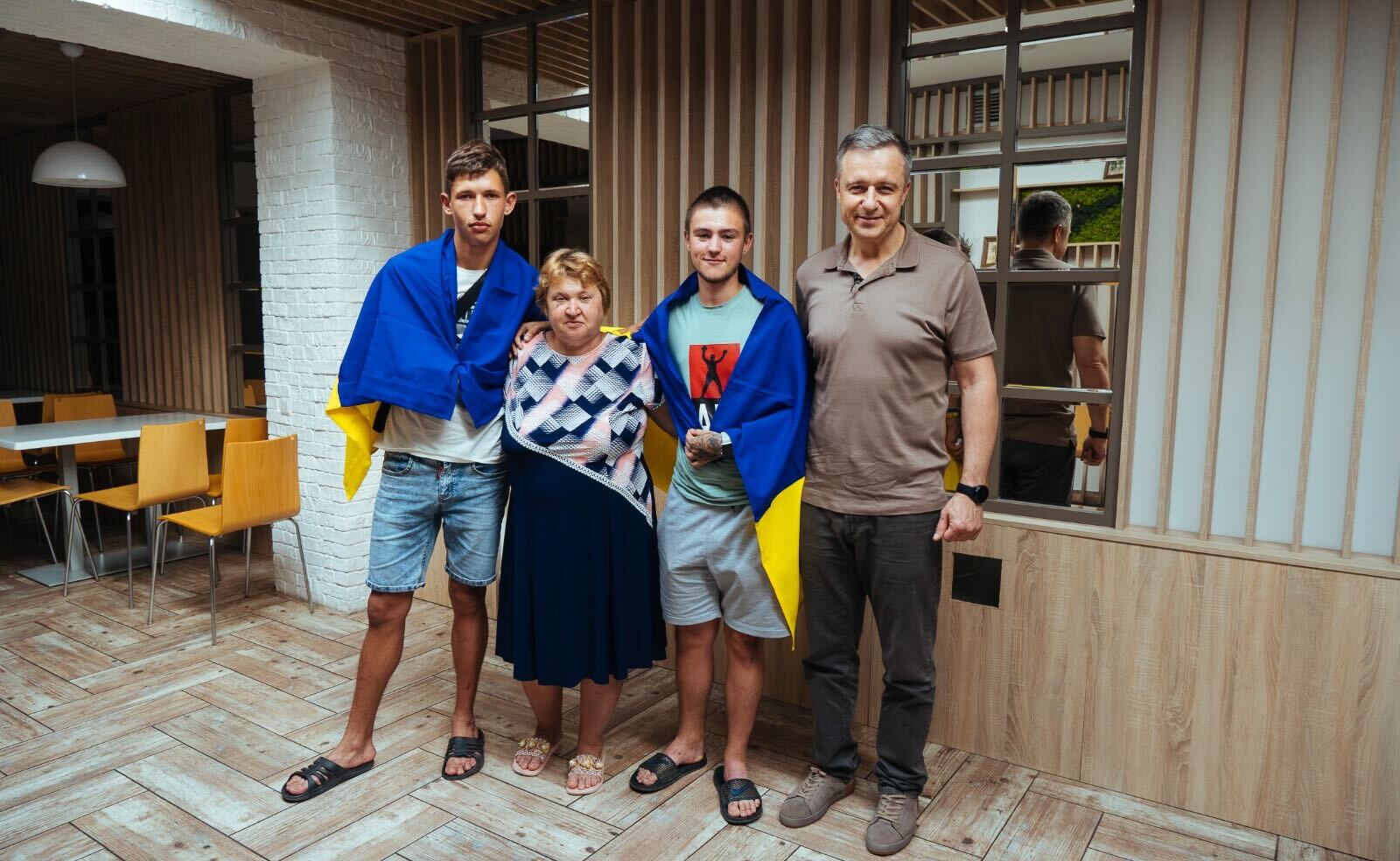 Teenagers Serhiy (left) and Denis Berezhnyi (centre right) stand at the Save Ukraine HQ in Kyiv with Mykola Kuleba (right) after being rescued from occupied Crimea in June 2023. Ukrainian flags are draped over their shoulders, as is custom for all children upon their return home