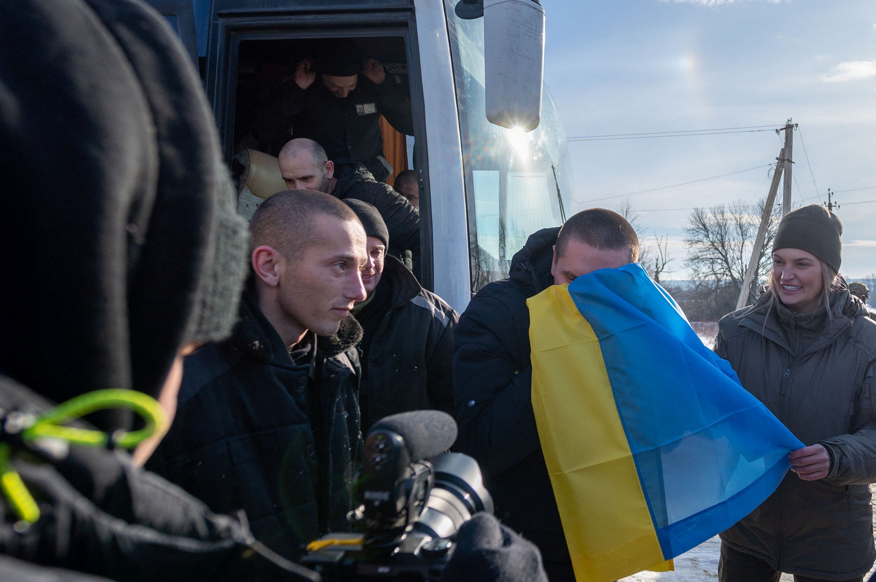 Dozens of Ukrainian PoWs, wearing black Russian prisoner uniforms, leave a bus as part of the swap