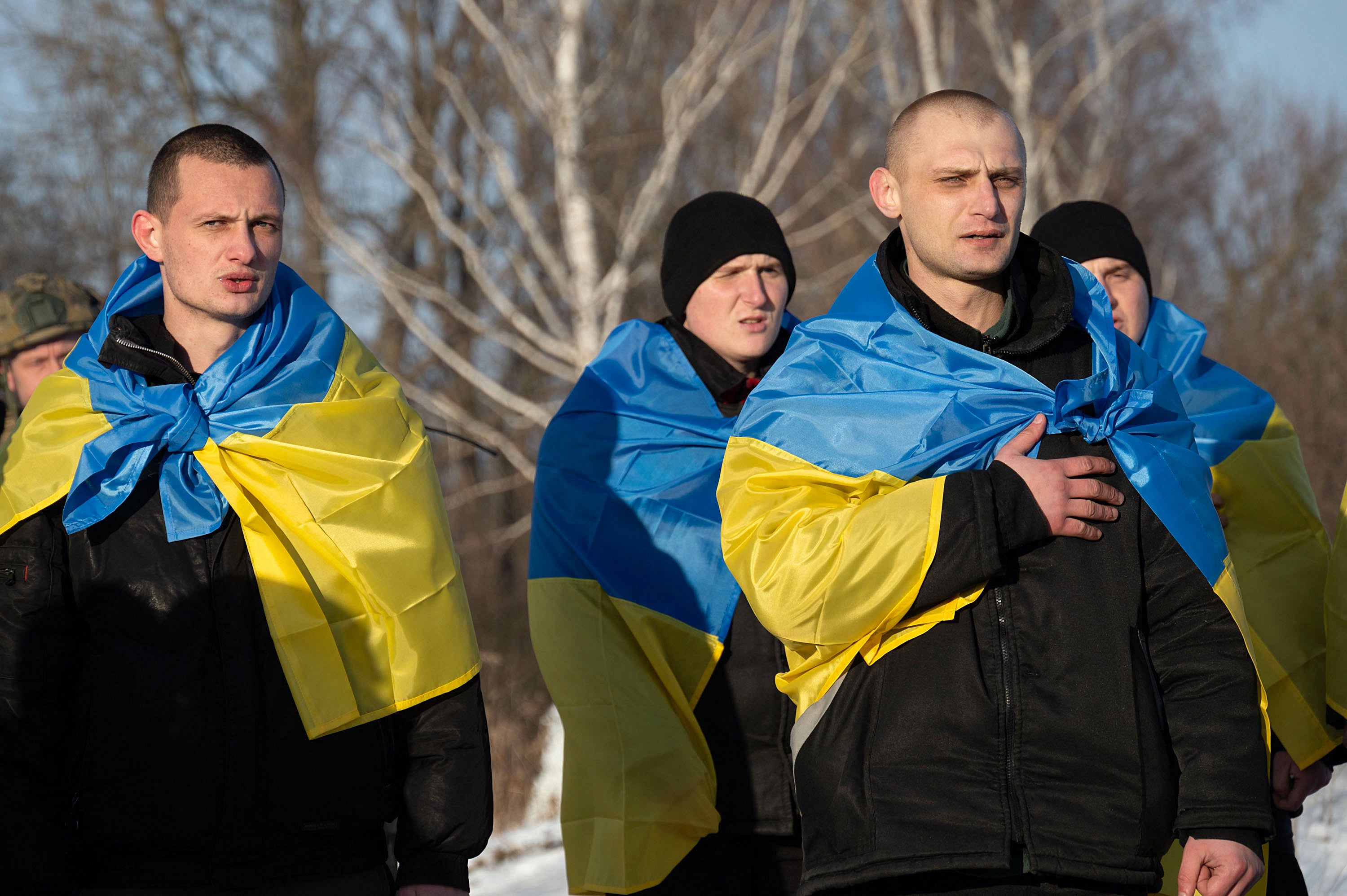 Ukrainian former prisoners of war wrapped in a Ukrainian flag and singing their national anthem, following a prisoner exchange