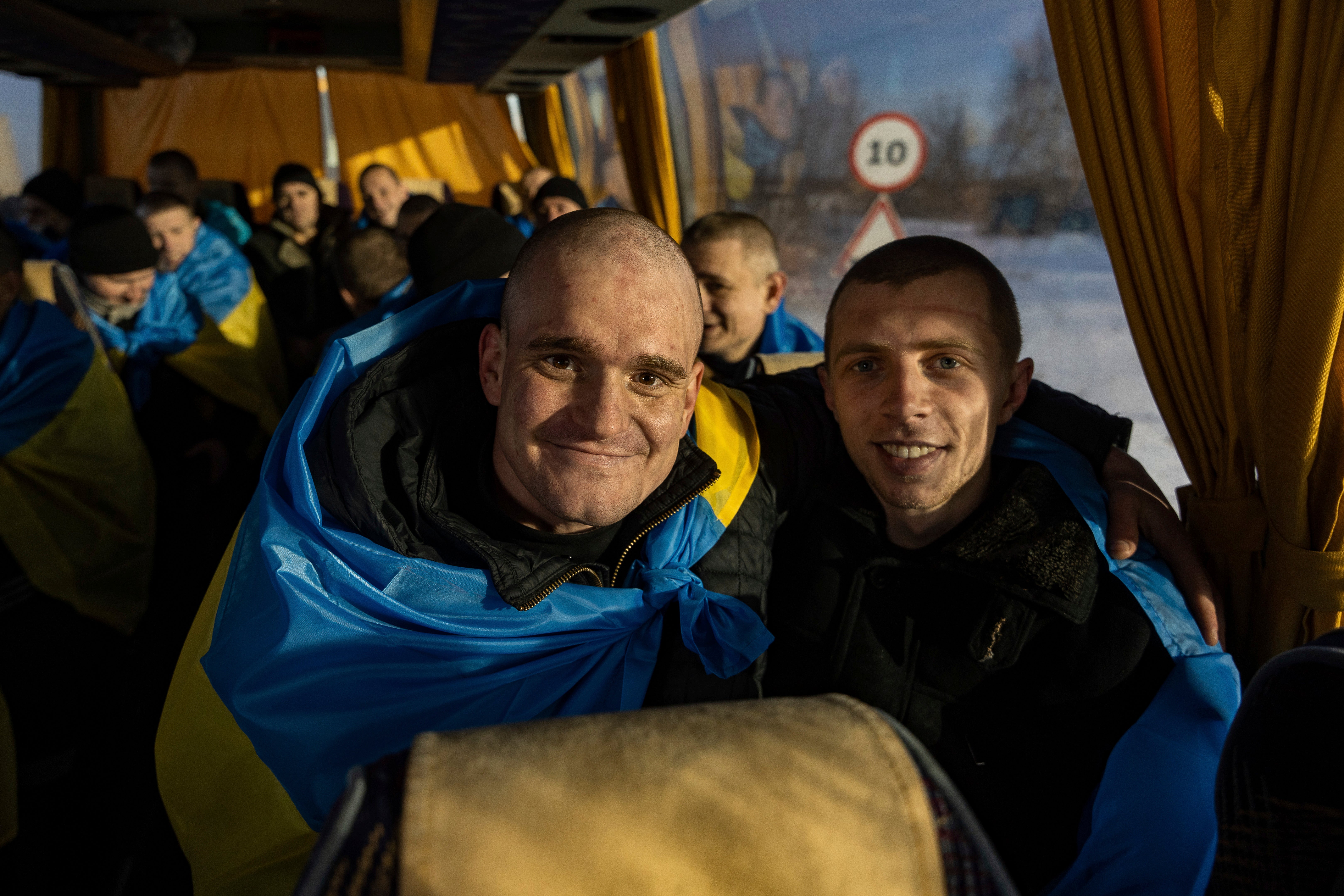 Recently swapped Ukrainian prisoners of war covered in national flags sit in a bus after a prisoner exchange on the Ukrainian Russian border
