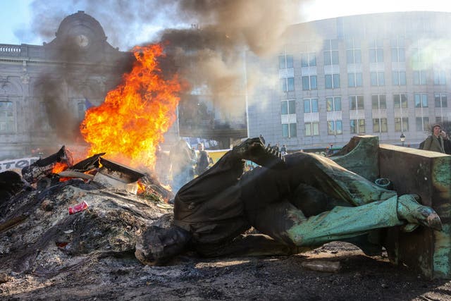 <p>The statue of John Cockerill lies on the ground as a fire burns during a protest by farmers in front of the European parliament  in Brussels</p>