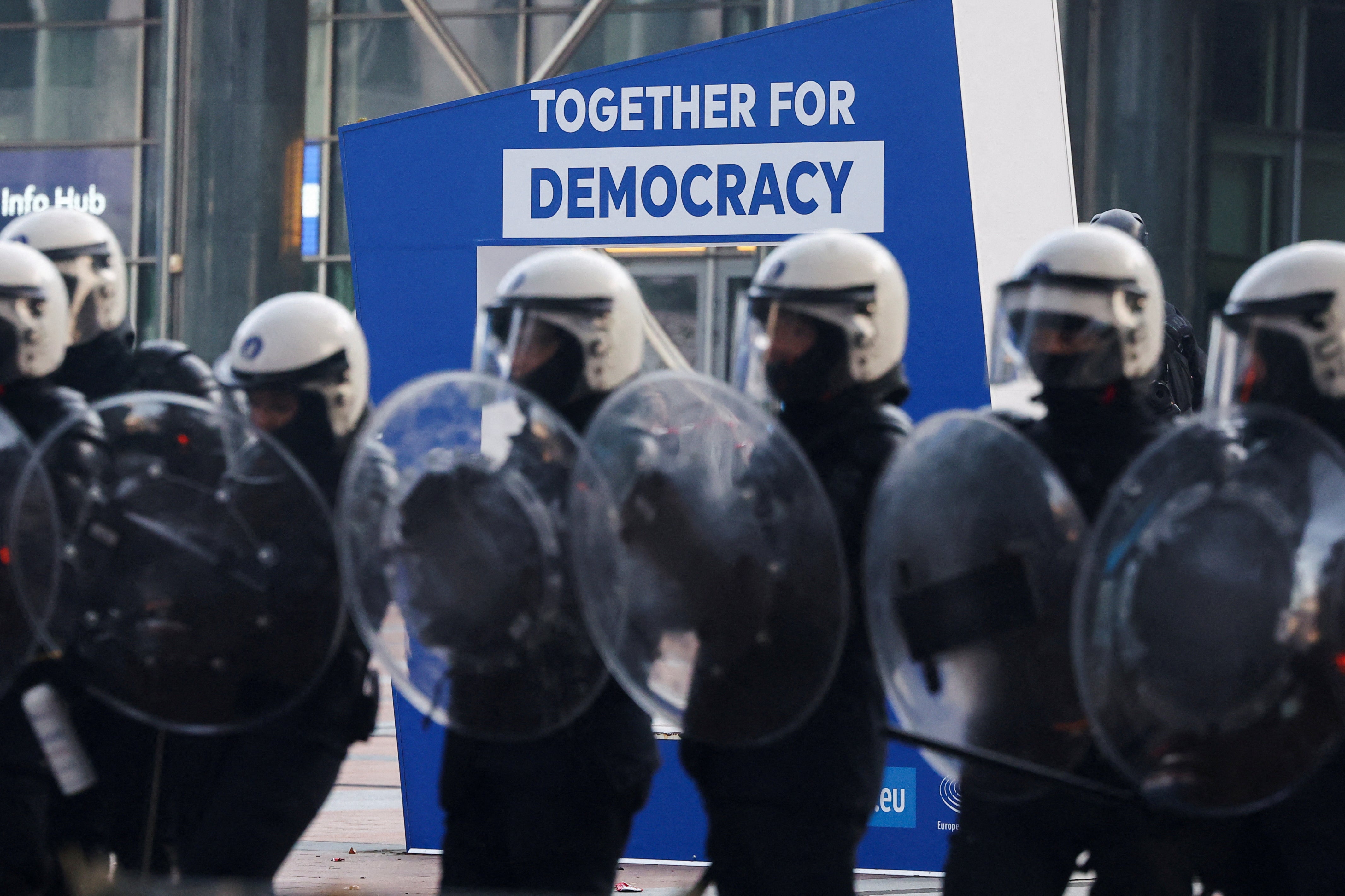 Police officers in riot gear stand guard in front of the European parliament