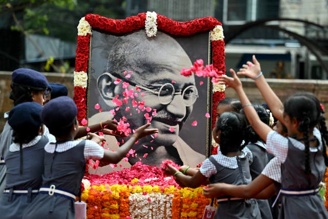 <p>Indian school children throws rose flower petals over a portrait of Mahatma Gandhi</p>