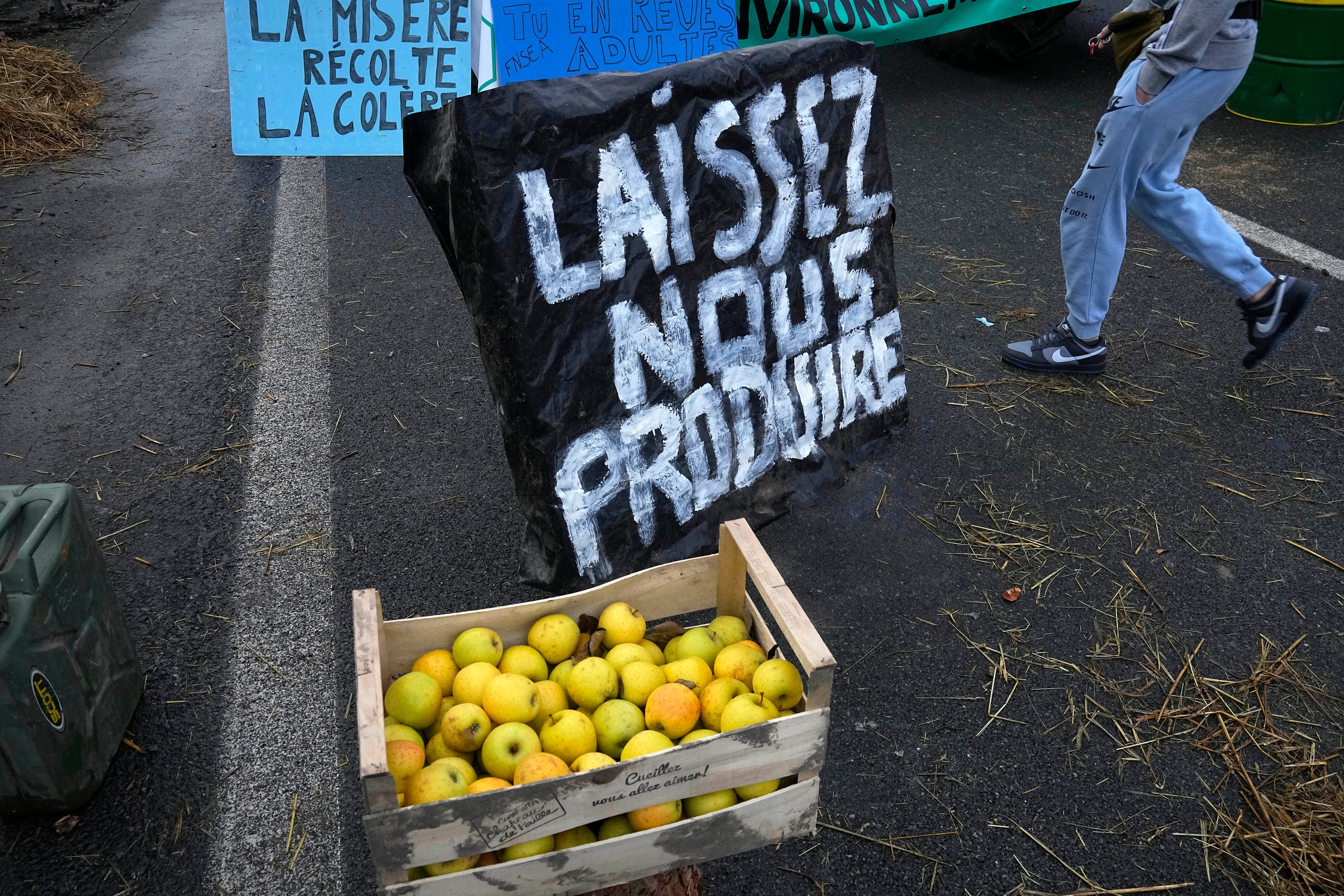 Apples are made available next to a poster reading ‘Let us produce’ as farmers block highways in France