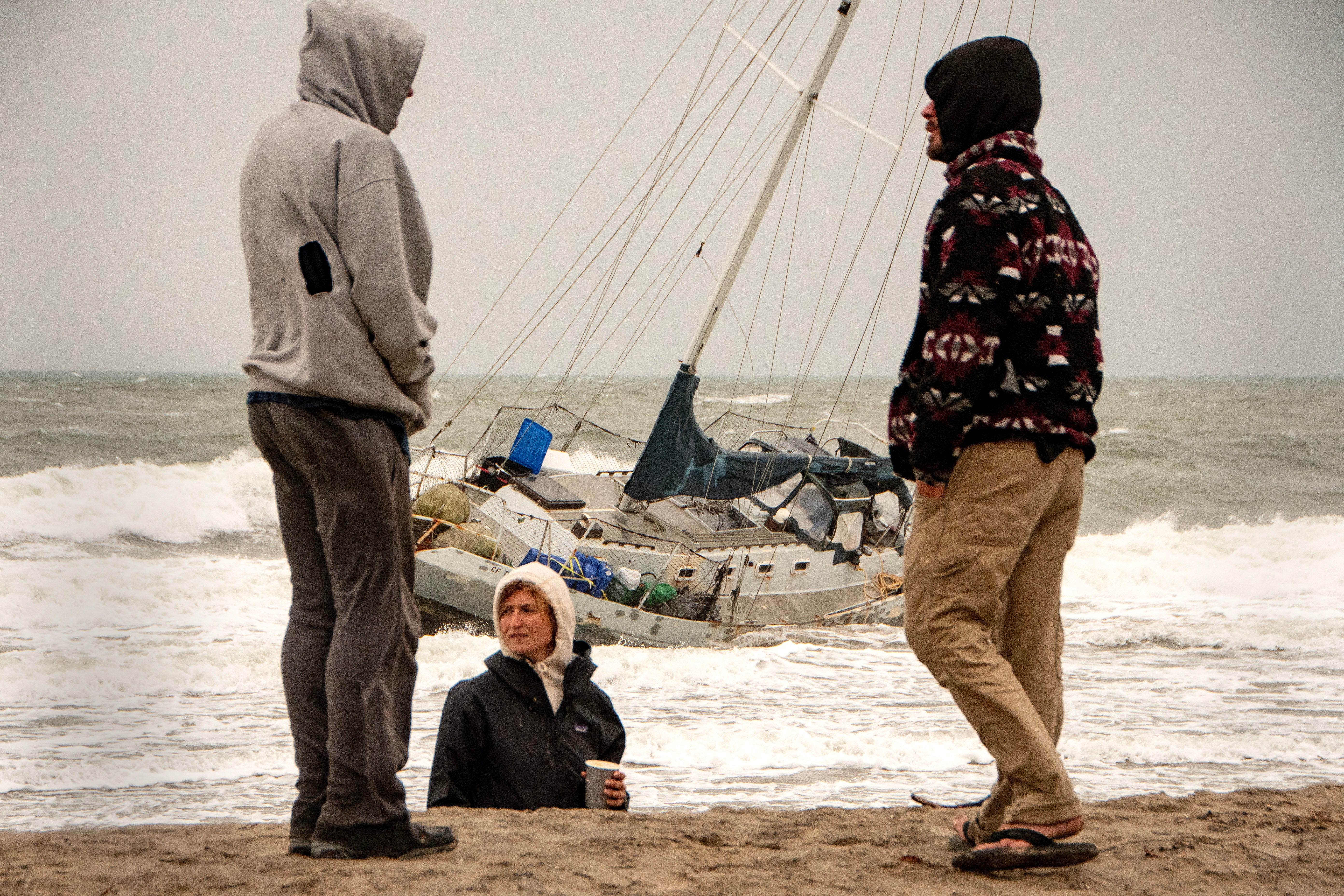 People stand next to a boat that washed ashore during an atmospheric river weather event in Santa Barbara, California