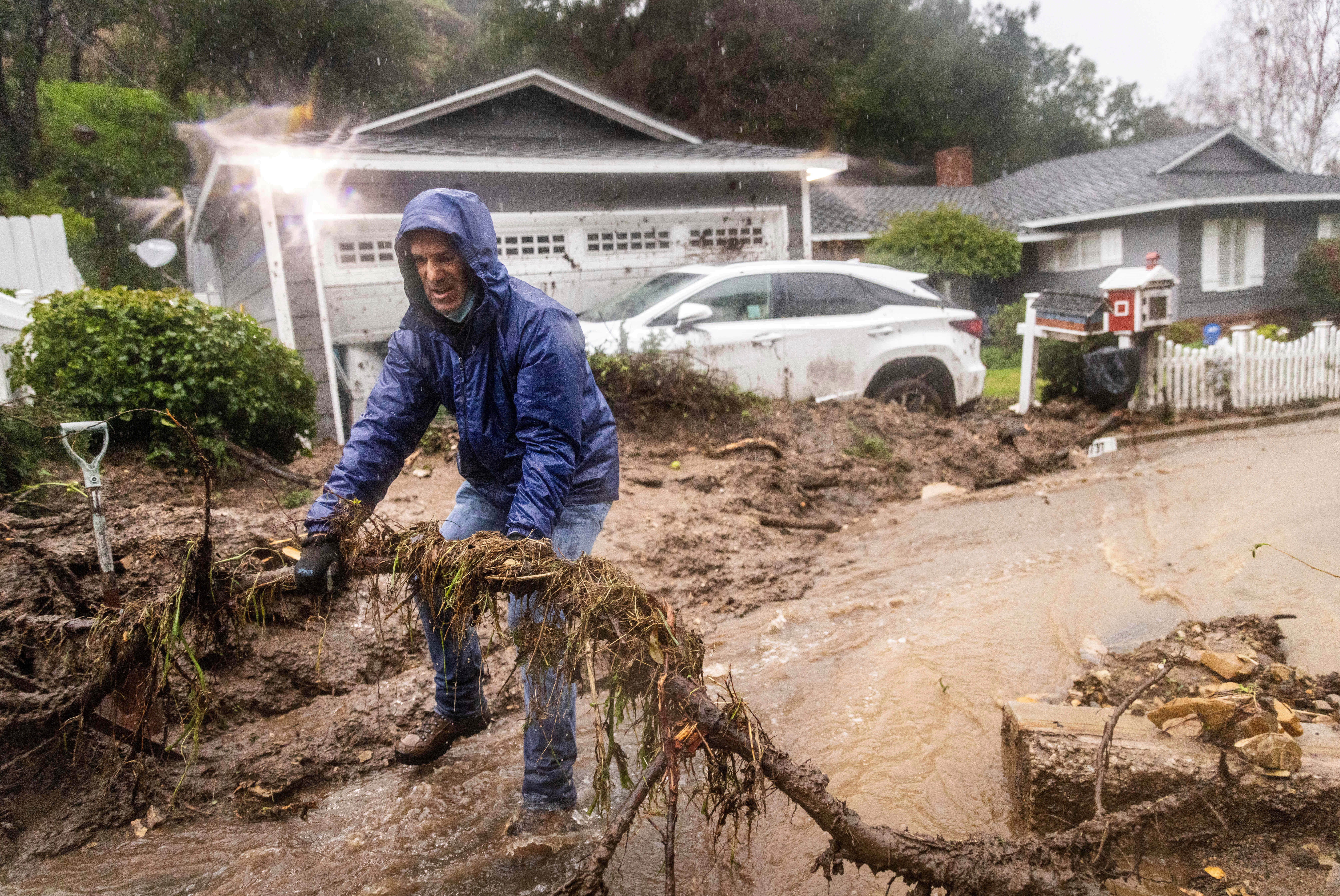 A man clears debris away from his house after a mudslide and flooding caused damage