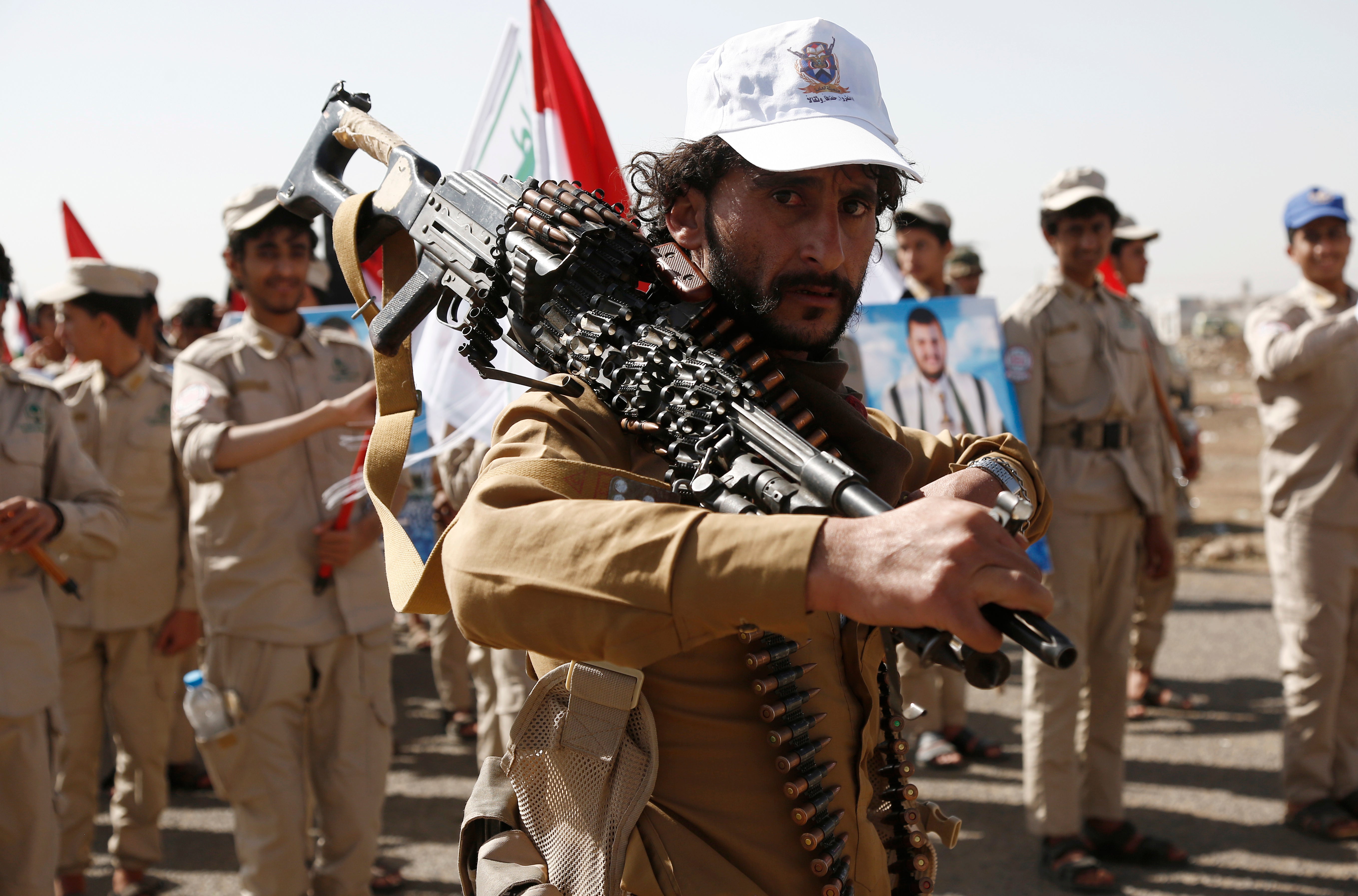A Houthi fighter carries a machine gun in front of scout team members carrying Yemeni and Palestinian flags