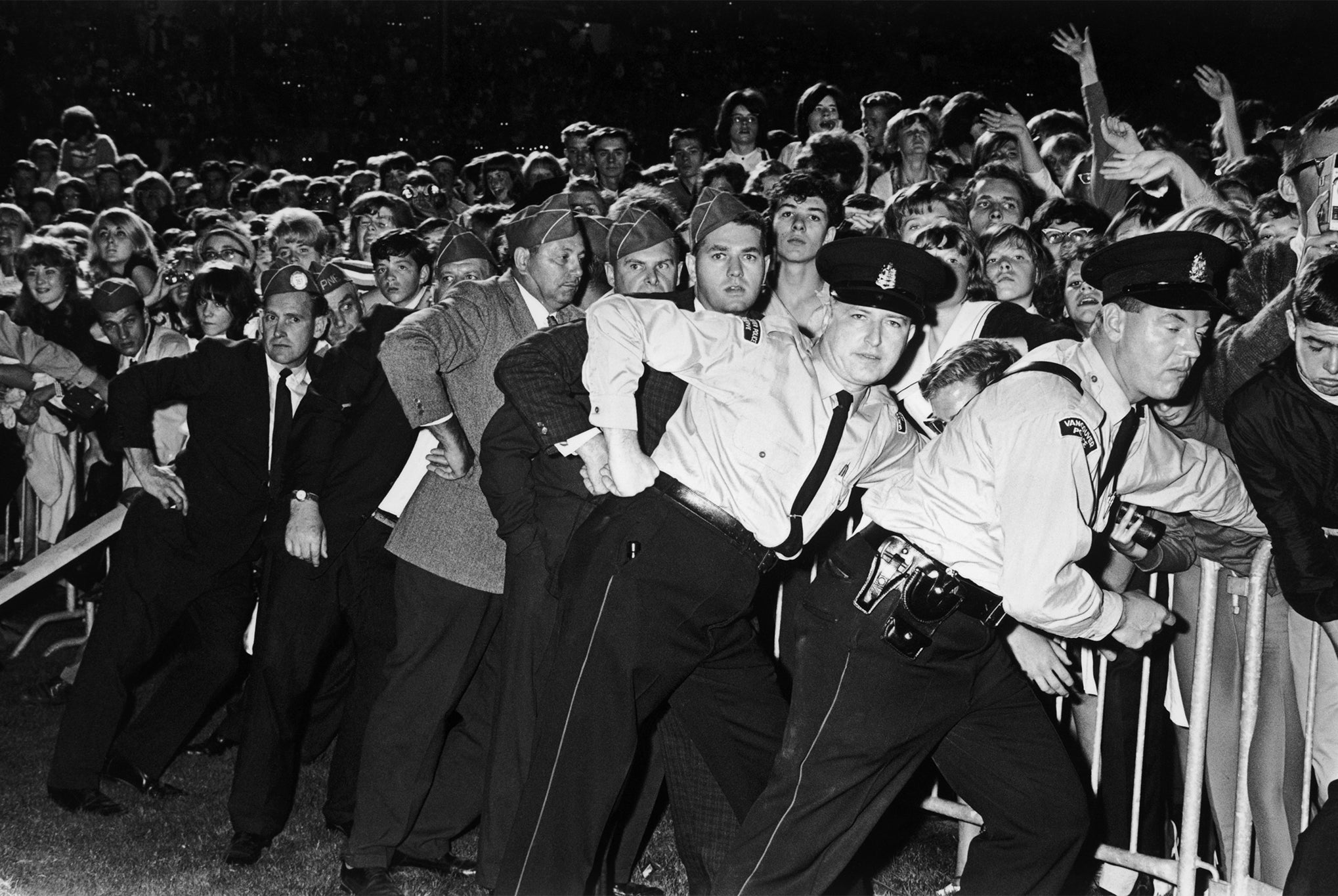Police and security guards hold back Beatles fans at a concert in Vancouver during the group’s North American tour in 1964