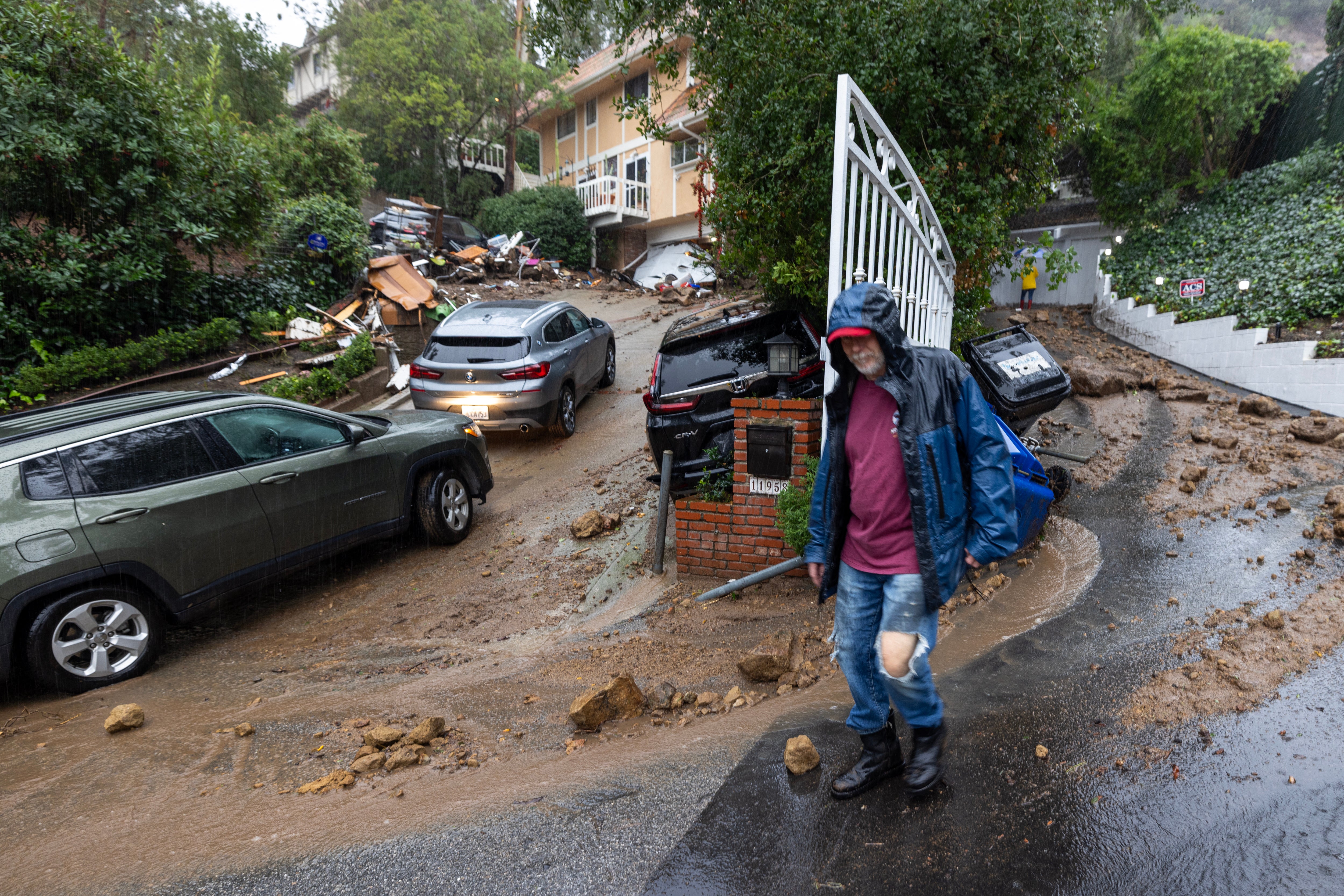 A man and several cars sit outside a home damaged by mudslides in Los Angeles, California on Monday