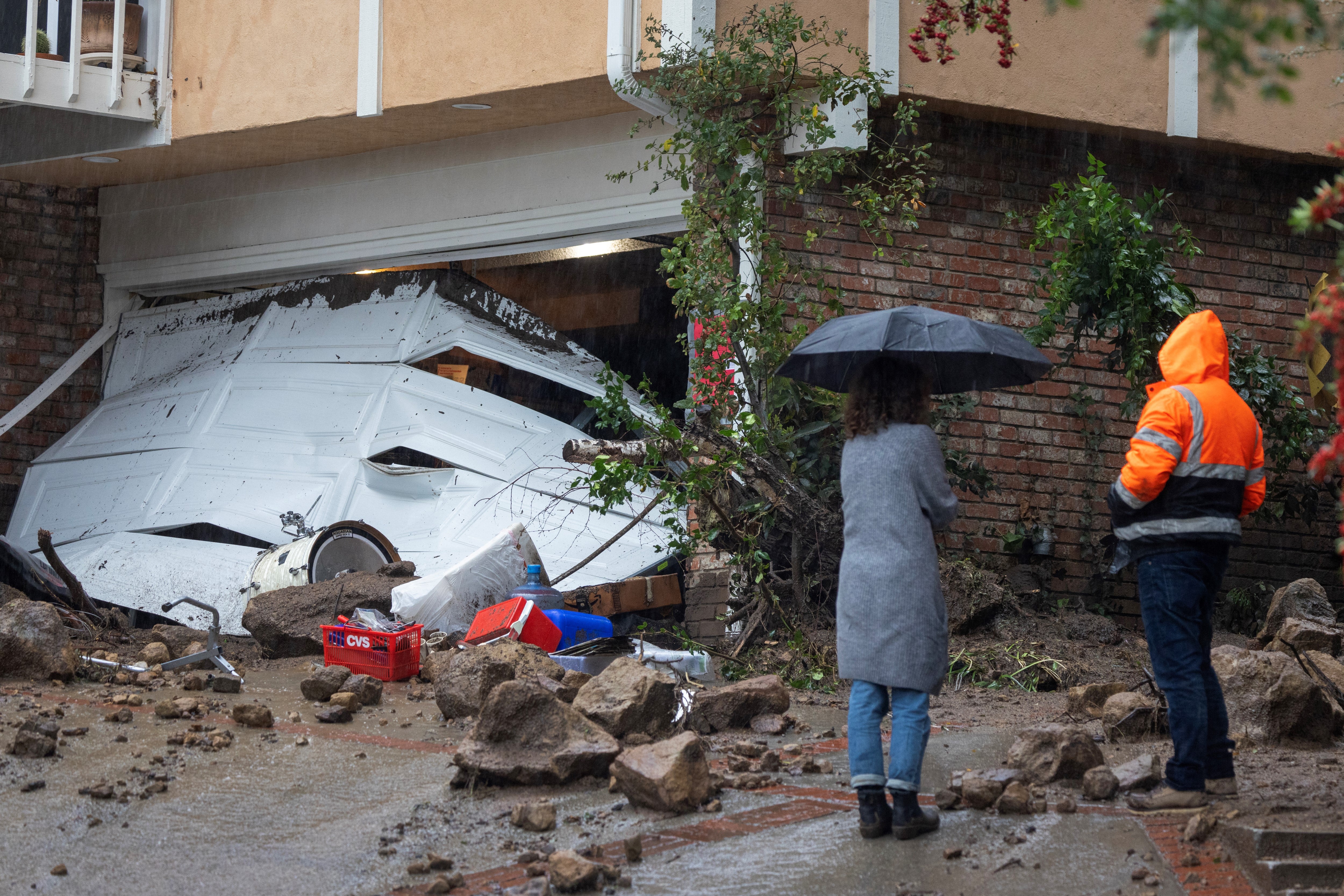 Two people stand outside a home damaged by a landslide in Los Angeles, California on Monday
